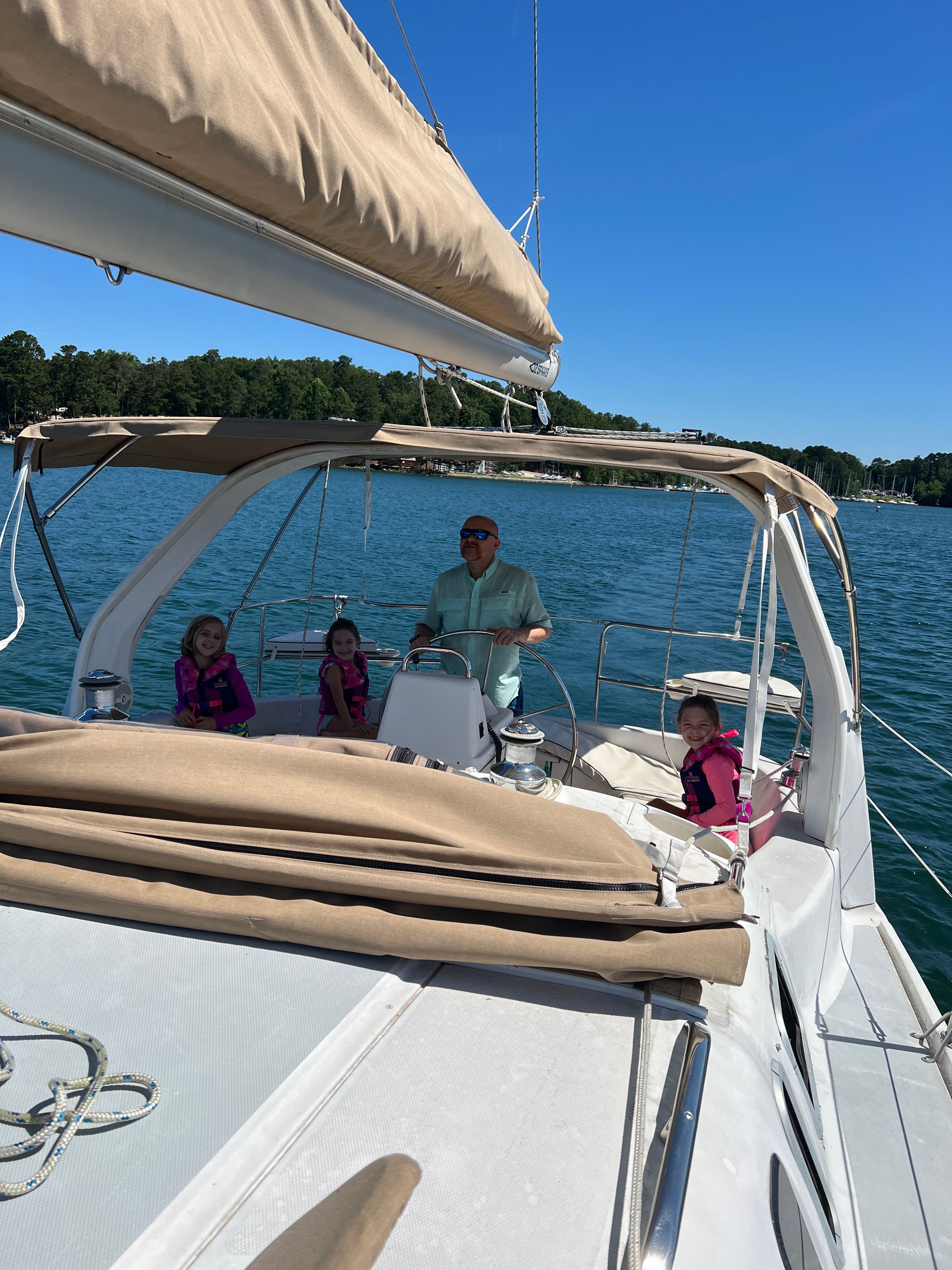 A man steers a sailboat with three children on board on a calm lake.