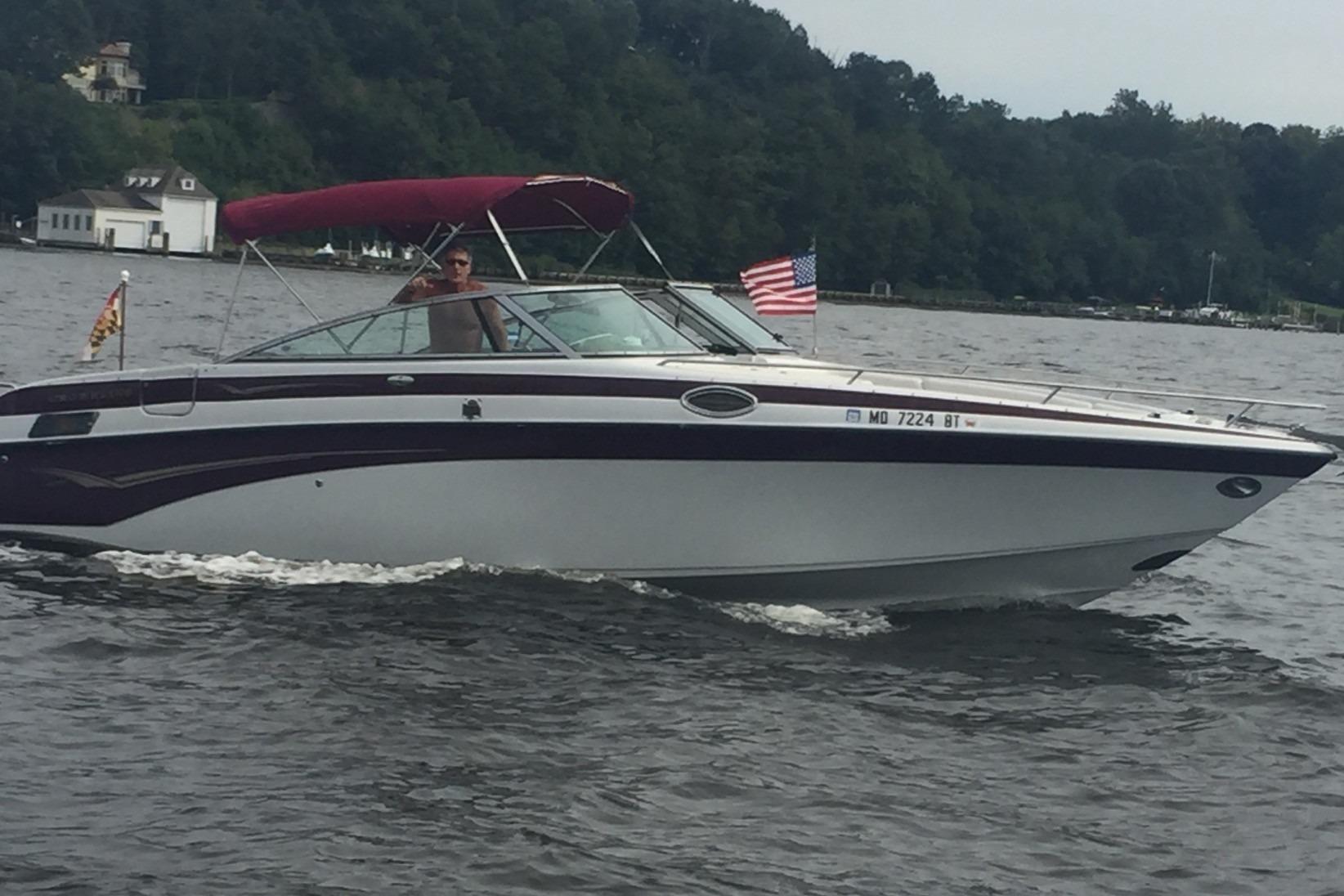 2004 Crownline 288 BR boat cruising on a lake with American flag.