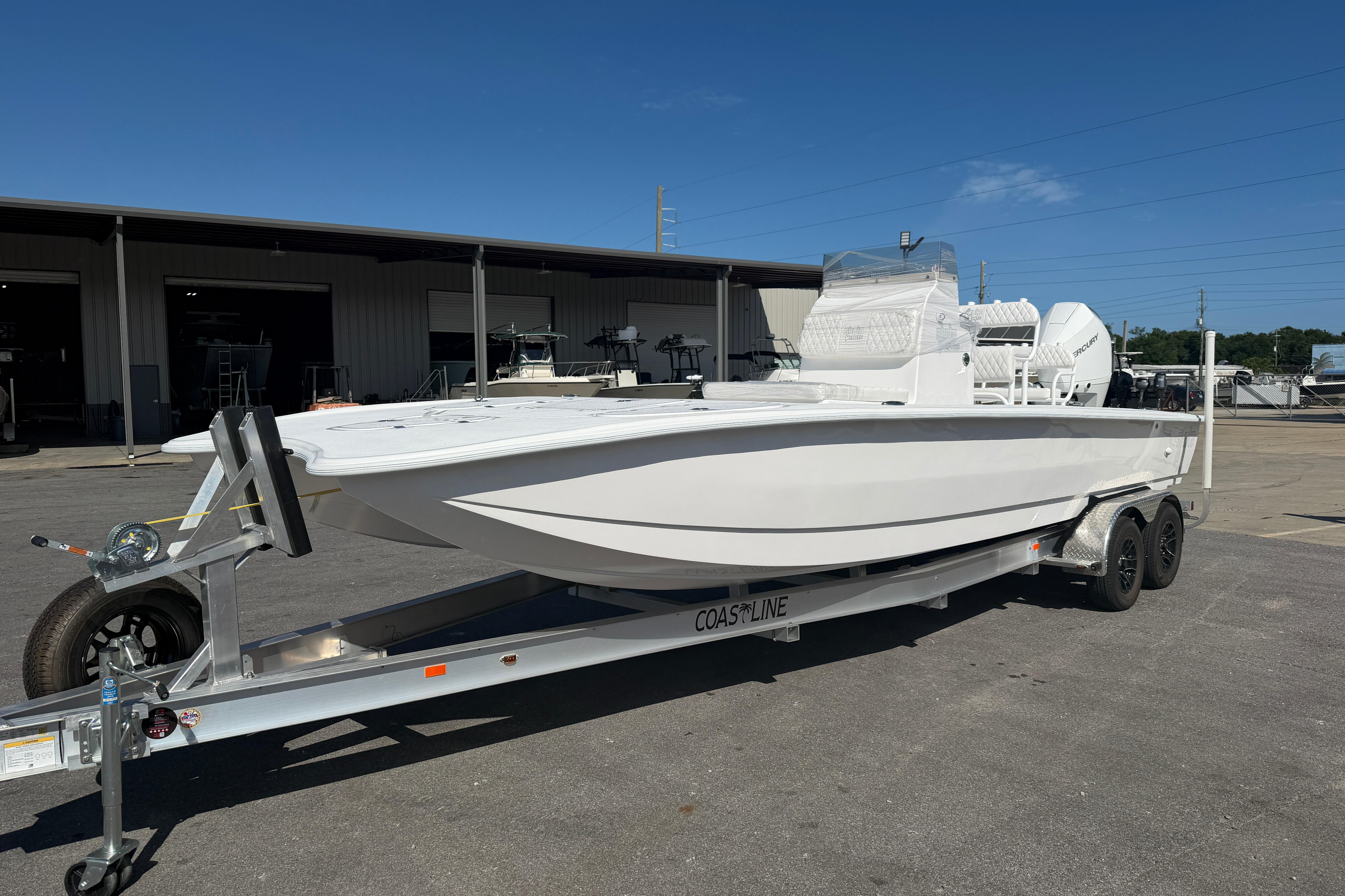2026 Skuta 24 Cat boat on trailer, parked outside a warehouse under clear blue sky.