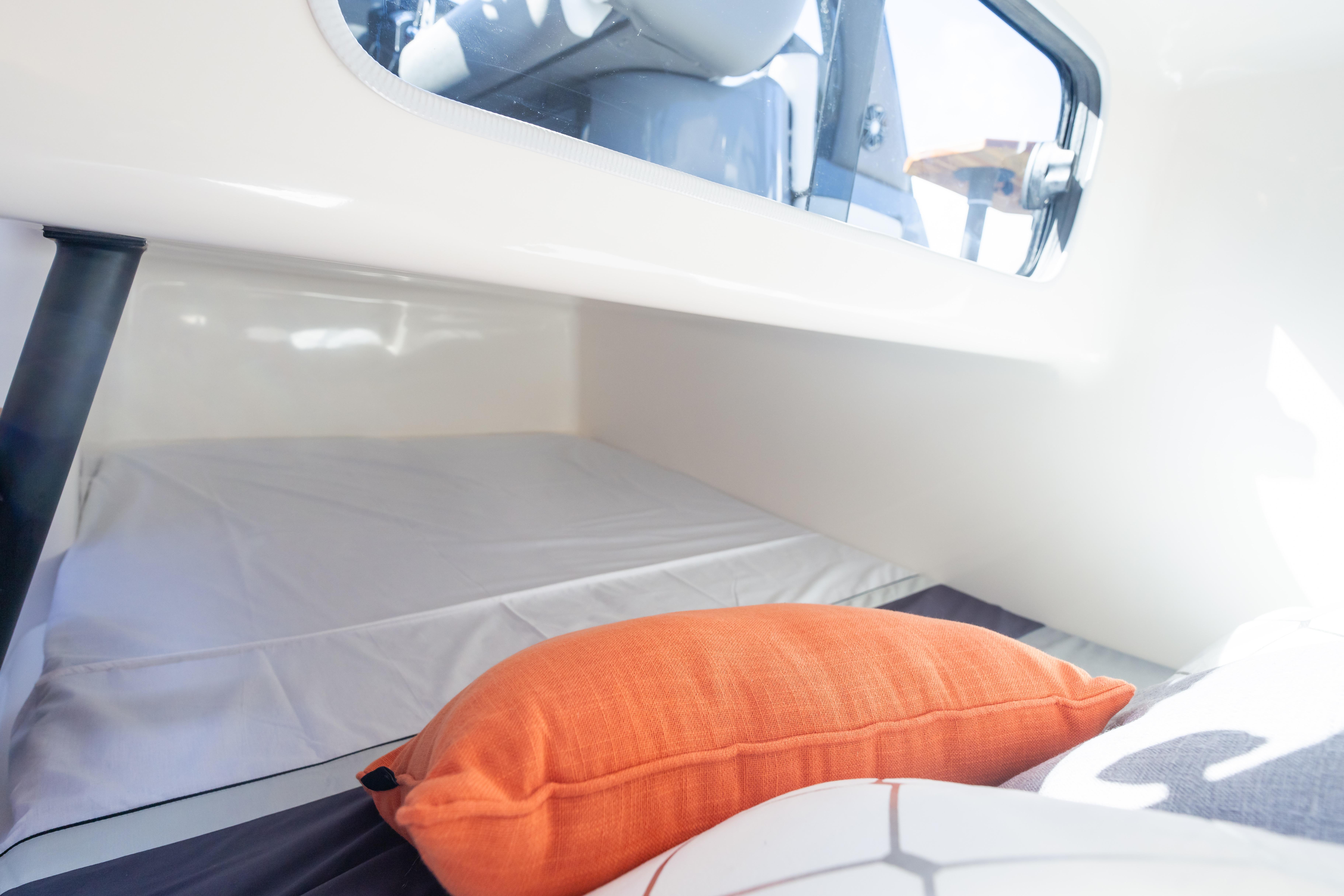 Cozy interior cabin of 2026 Hanover 305 boat with orange pillow and window view.