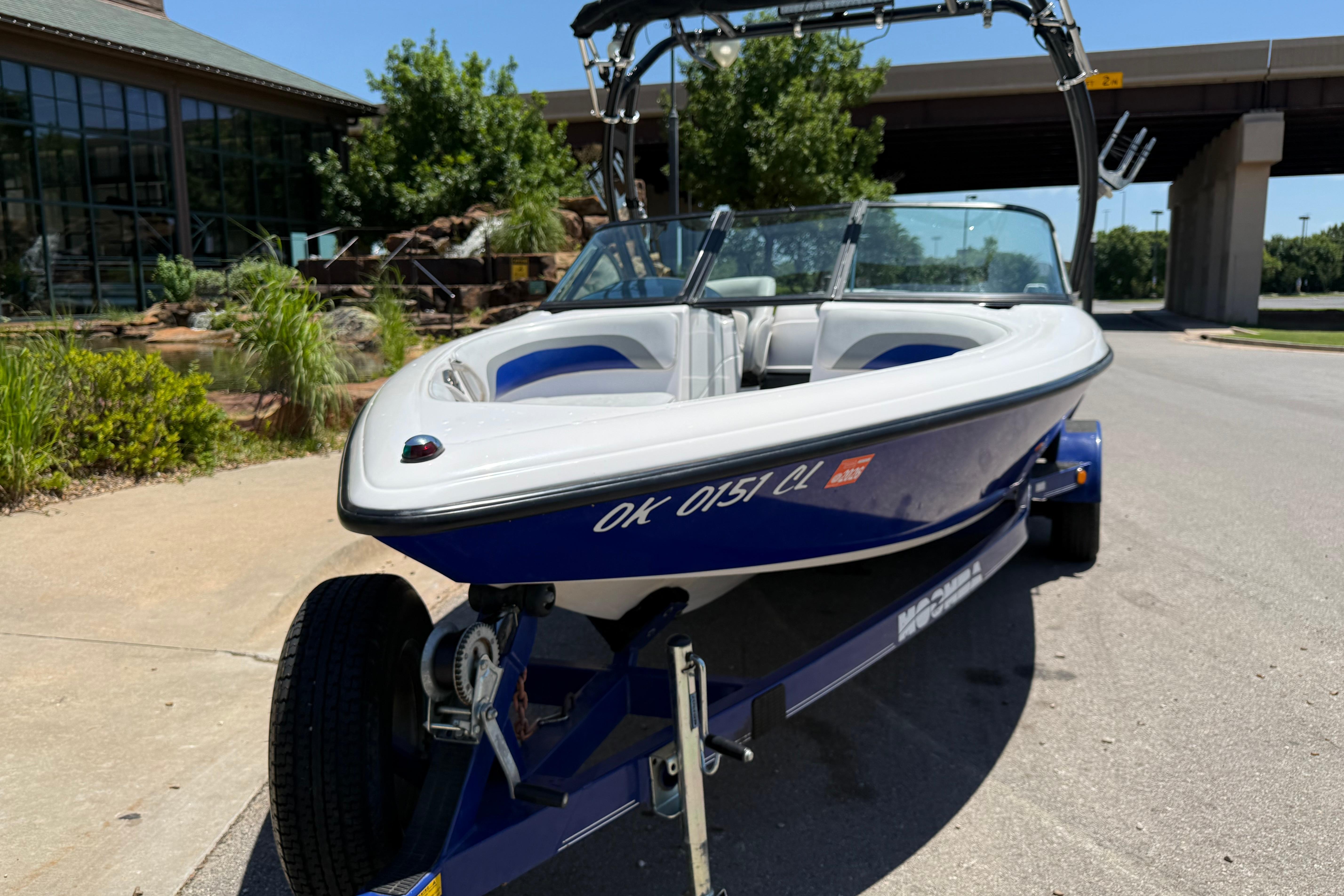2001 Moomba Outback boat on trailer, parked outdoors near a building and greenery.