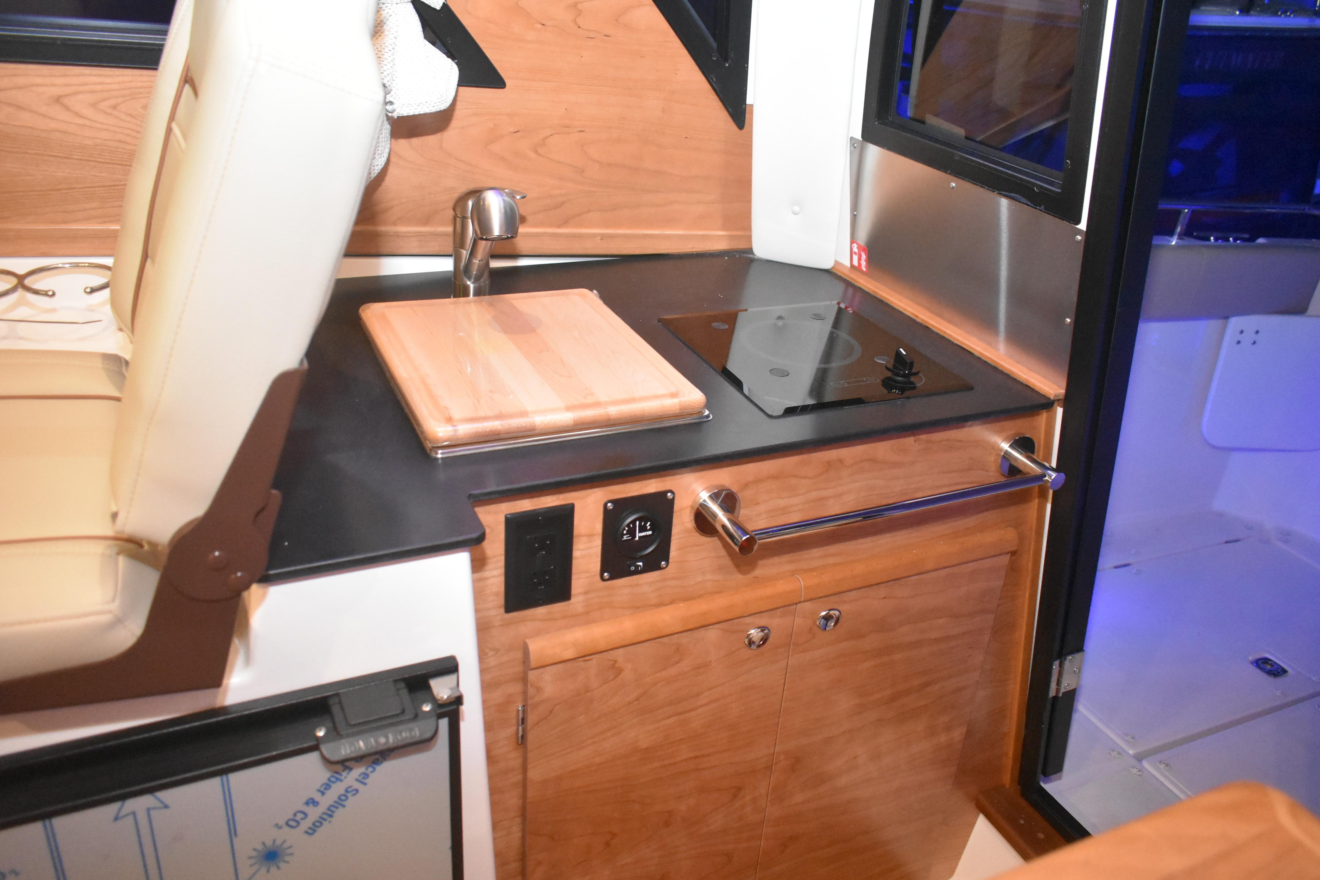 2026 Cutwater C-248 Coupe interior kitchen with stove, sink, and wooden cabinetry.