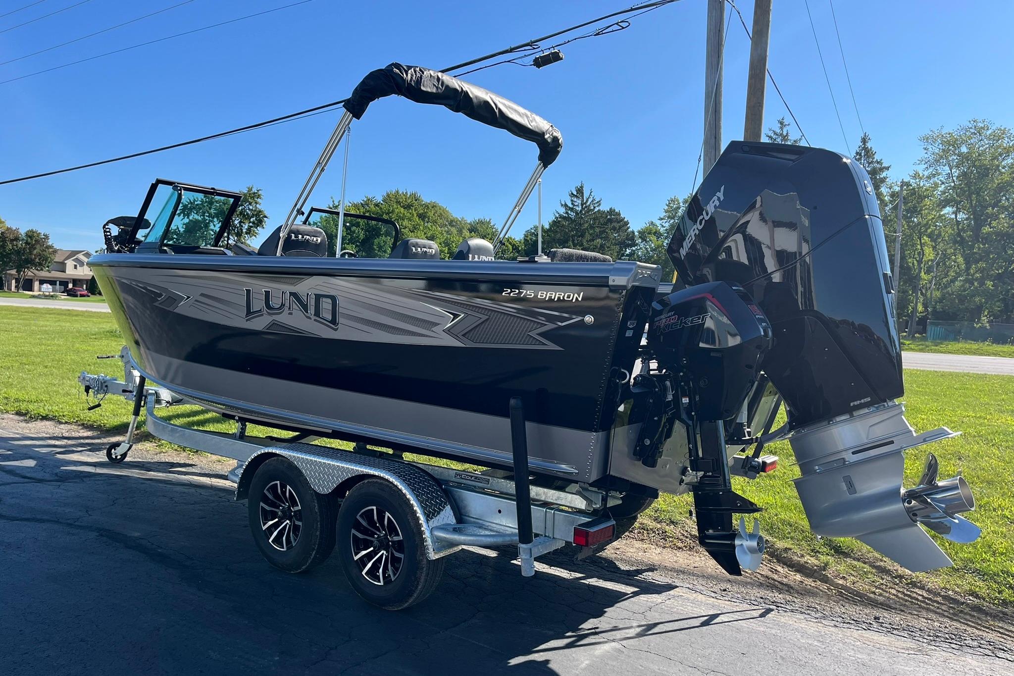 2026 Lund 2275 Baron boat on trailer, parked outdoors, featuring a powerful Mercury engine.