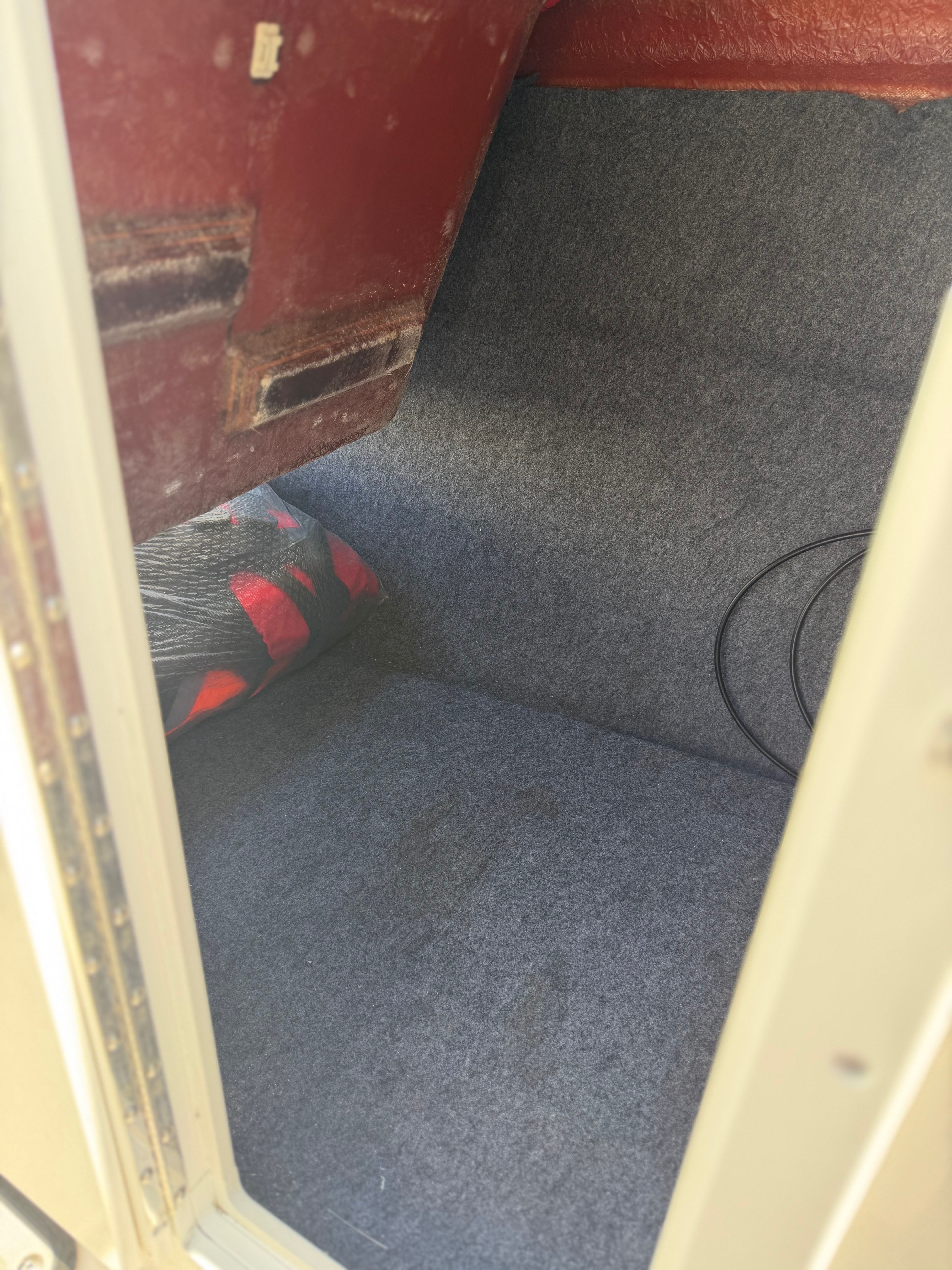 Interior of a boat with gray carpeted floor and a cushion.