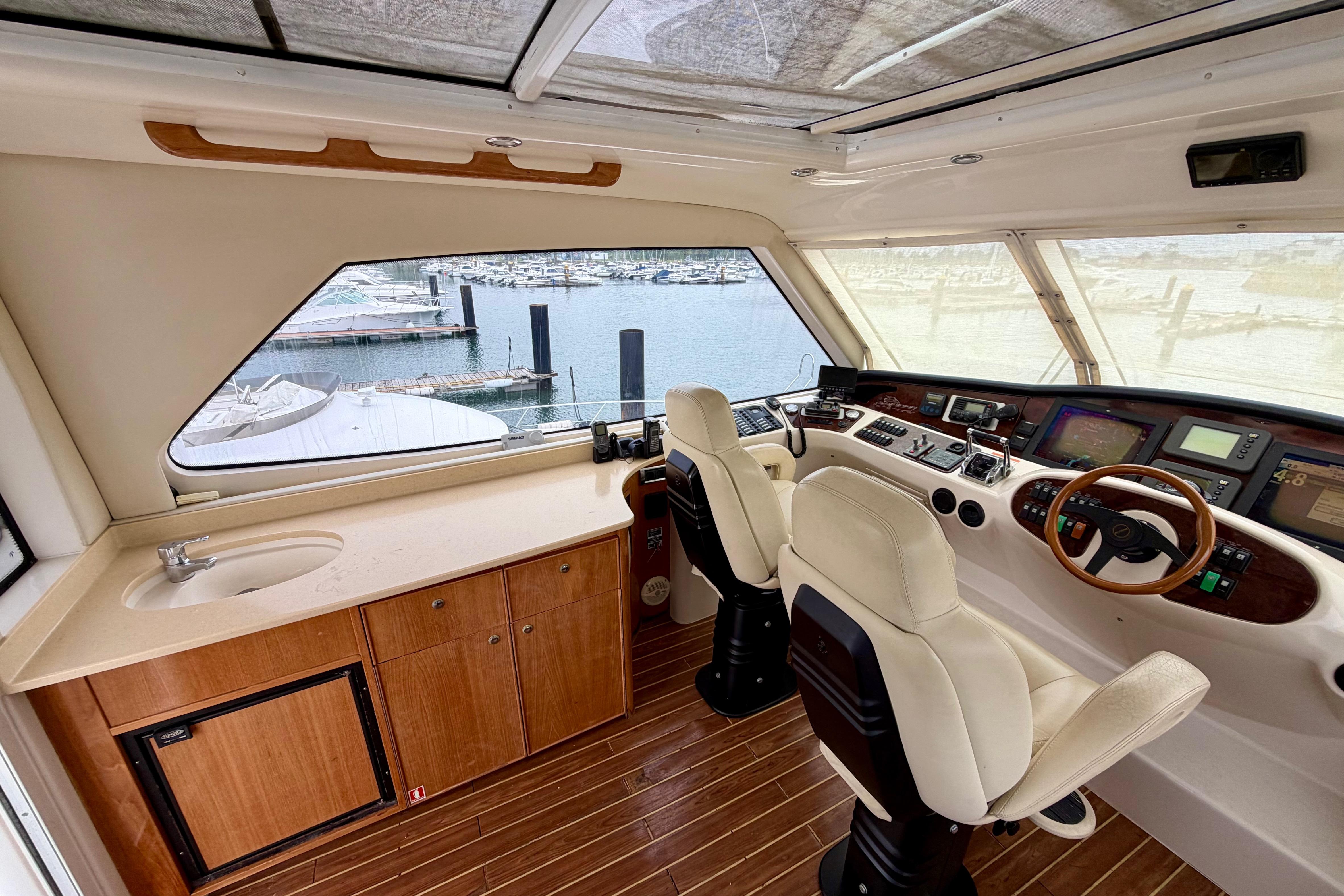 Luxurious 2003 Riviera 60 Flybridge yacht interior with helm, controls, and marina view.