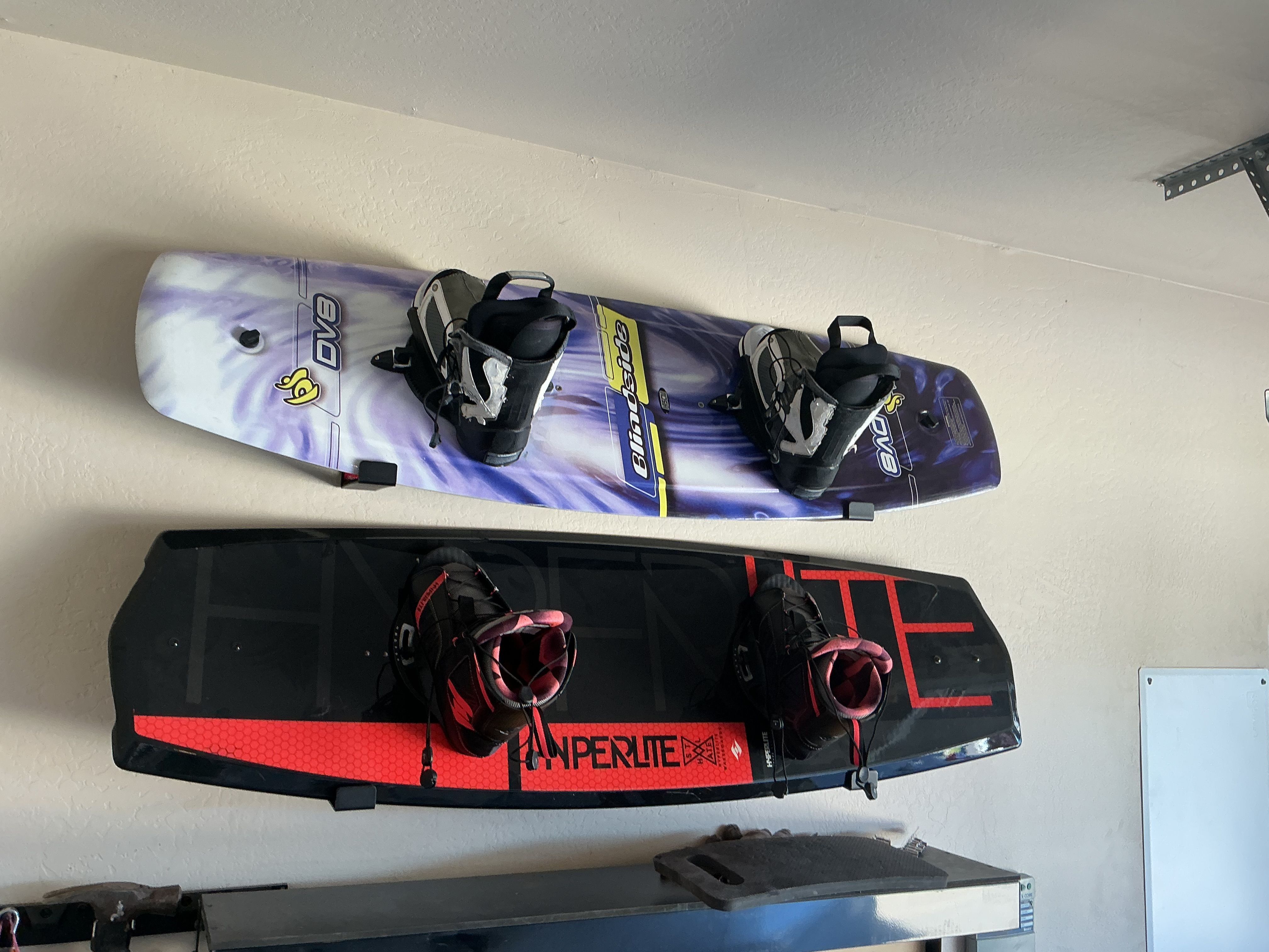 Two wakeboards are mounted on a wall, one in purple and white, the other in black and red.