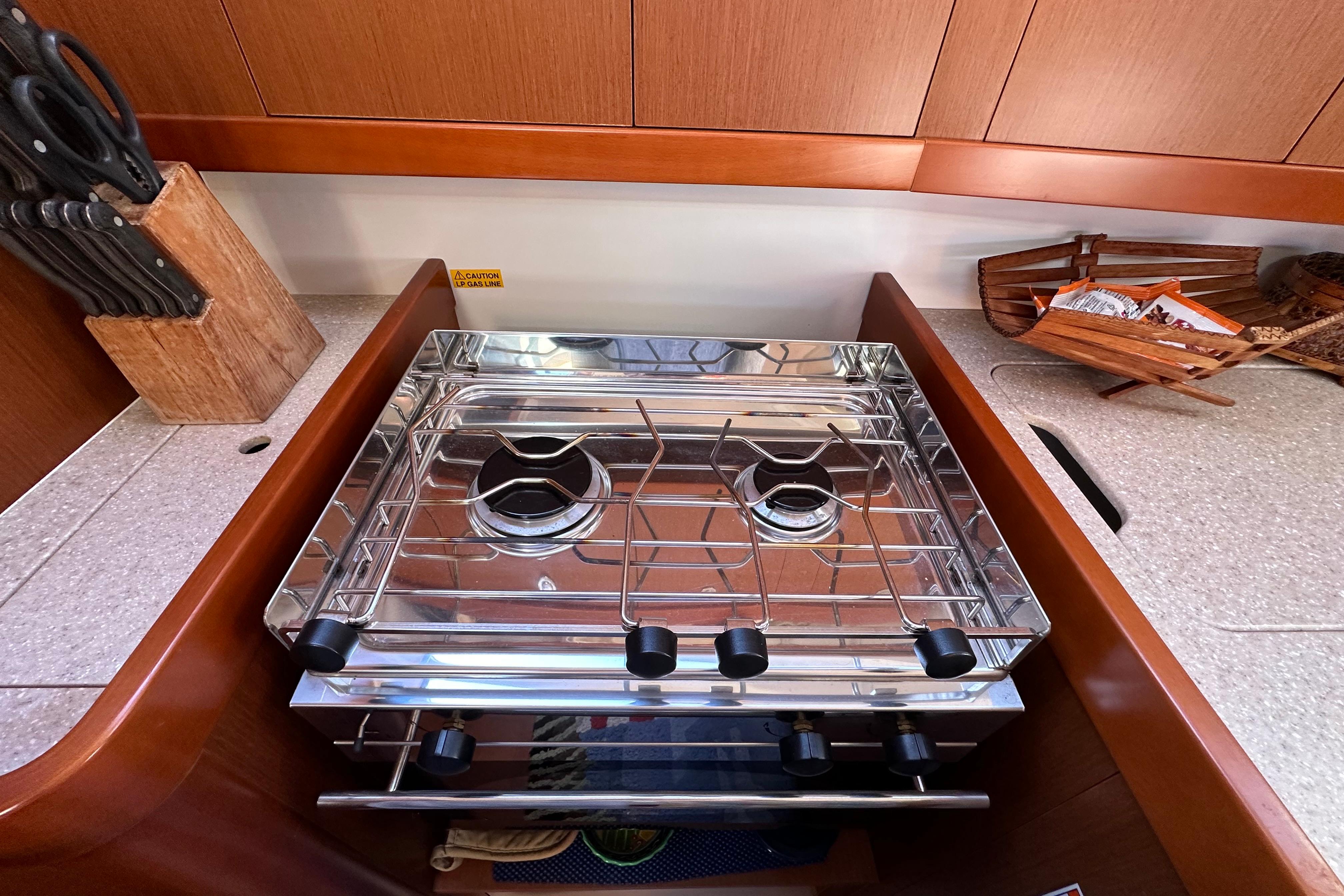 Compact kitchen stove on 2015 Beneteau Oceanis 37 yacht with wooden cabinetry and knife block.