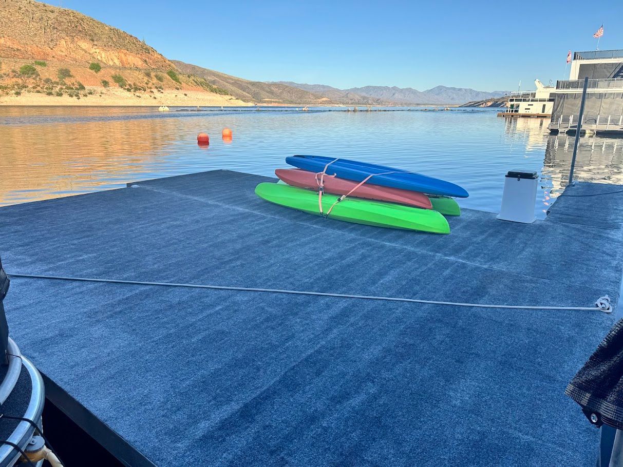 Kayaks on a dock beside a Summersun houseboat, calm lake in the background.
