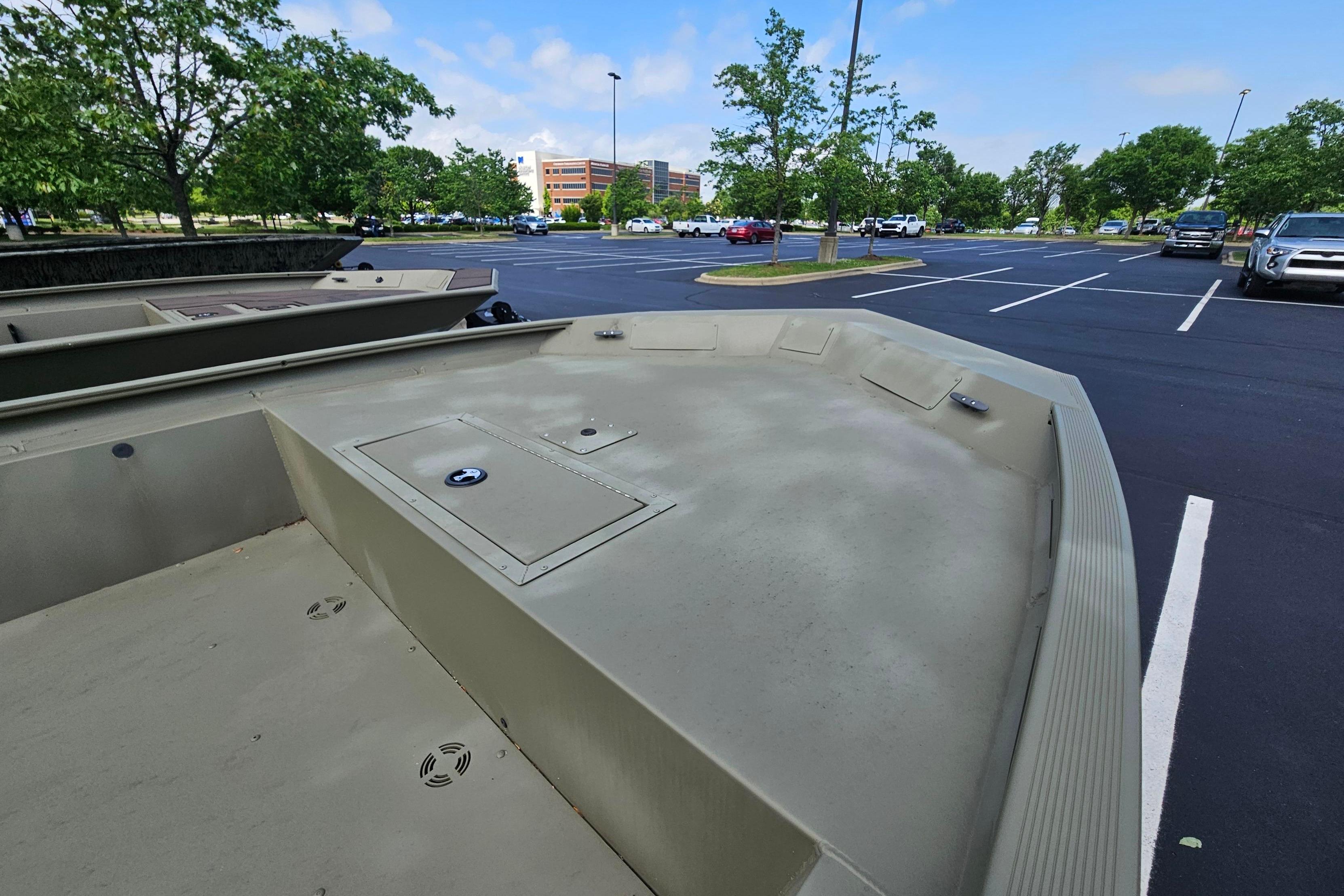 2025 Tracker Grizzly 1860 Utility boat in a parking lot, surrounded by trees and vehicles.