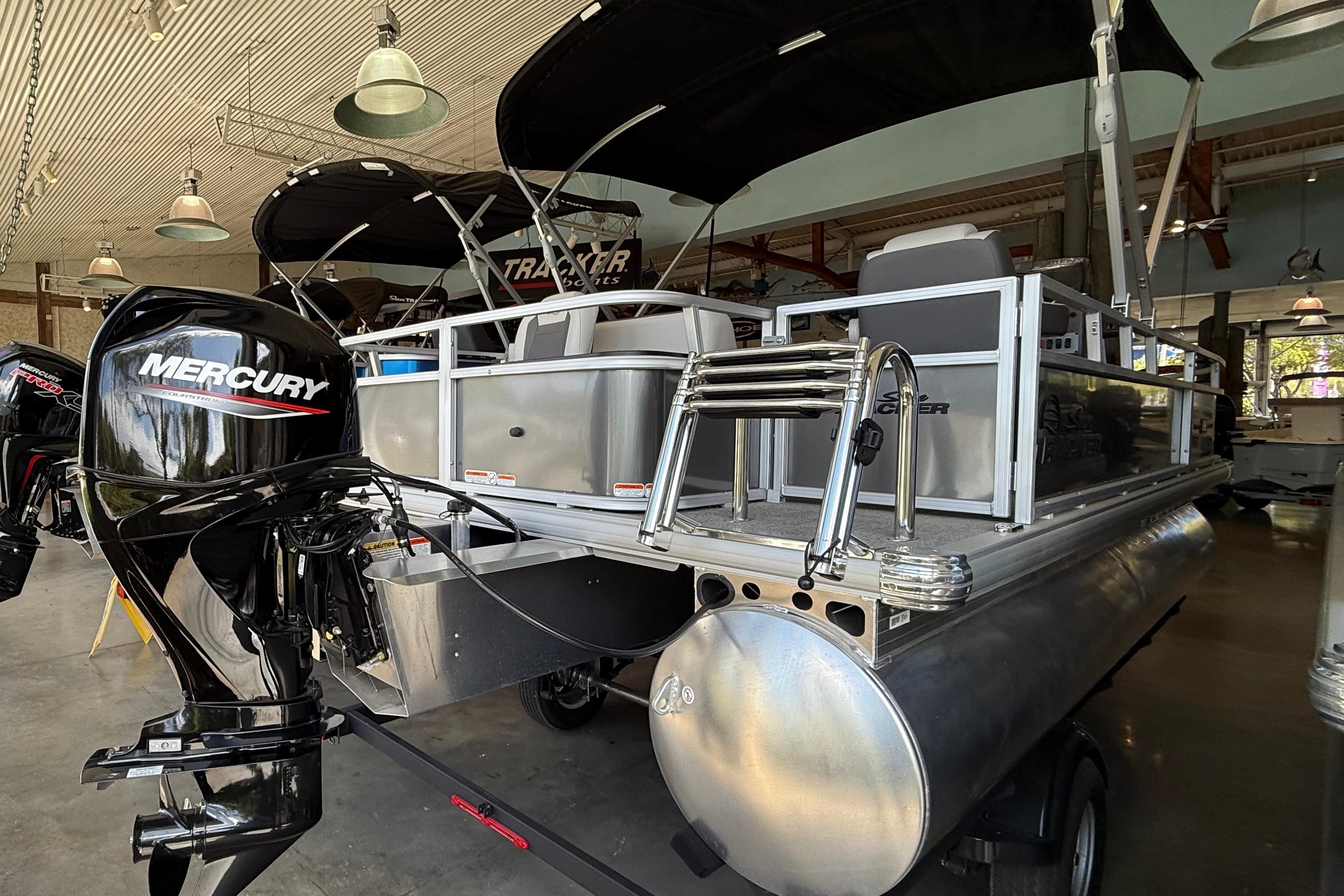2026 Sun Tracker Bass Buggy 18 DLX pontoon boat with Mercury outboard motor in showroom.