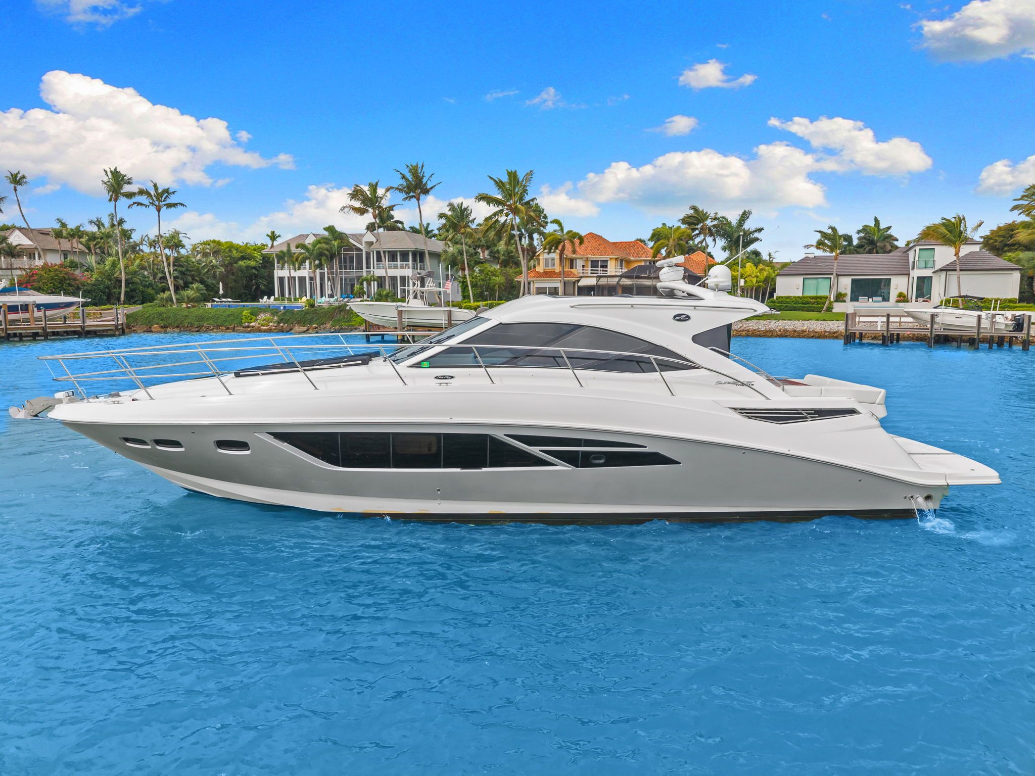 A 2017 Sea Ray Sundancer 510 cruising on blue water, surrounded by palm trees and houses.