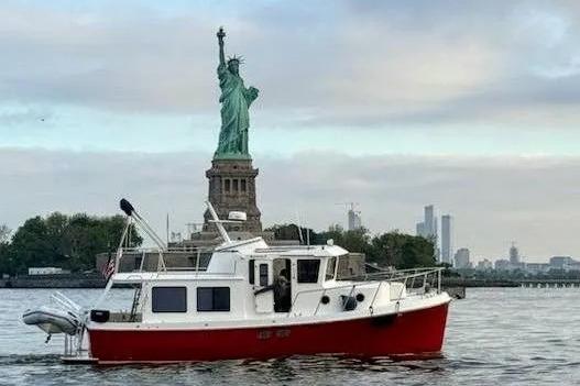 2006 American Tug AT boat near Statue of Liberty, New York City skyline in background.