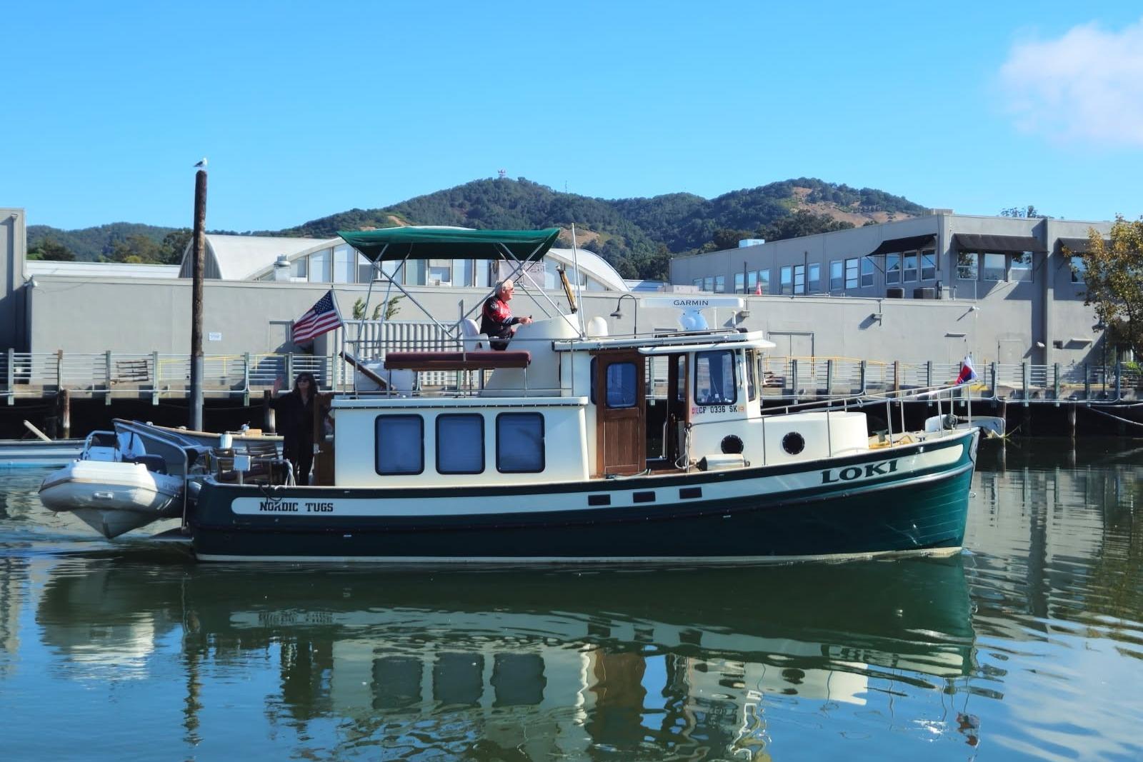 1996 Nordic Tug 32 boat named "Loki" docked in a marina with scenic background.