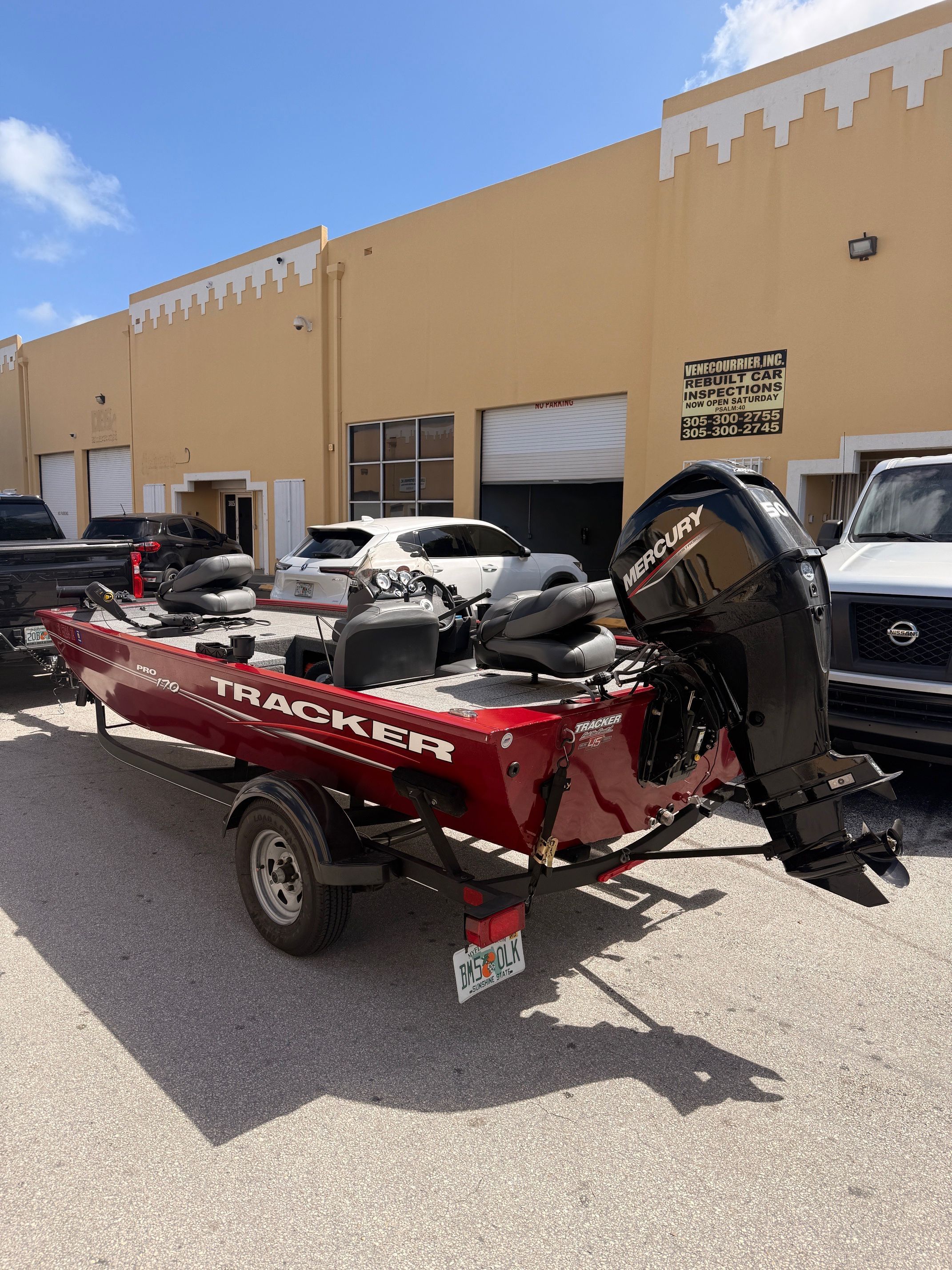A red Tracker Pro 170 boat is on a trailer in front of a building.