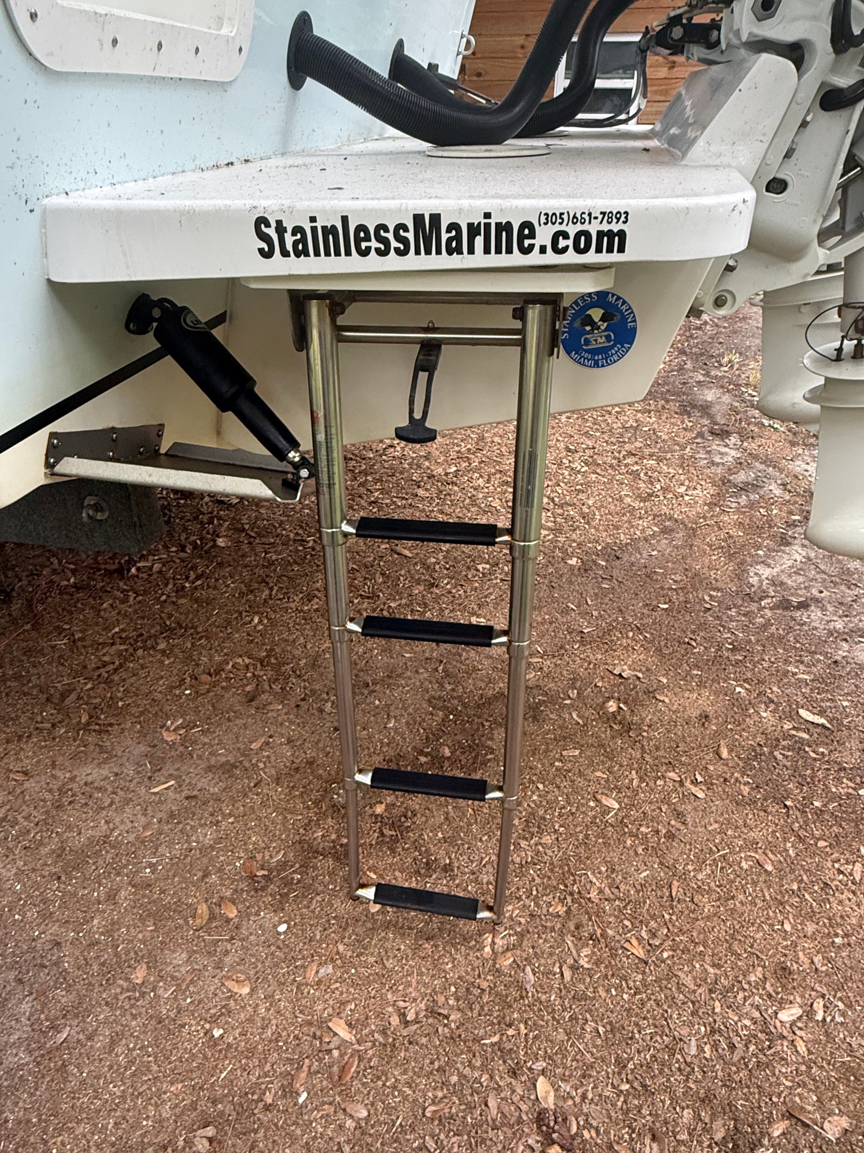 A stainless steel ladder is mounted on the stern of a boat, which is on dry ground.