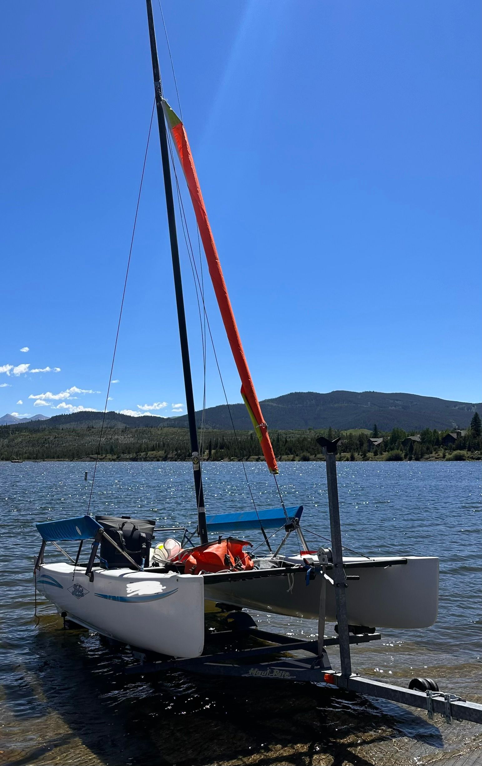 A 2007 Hobie Cat Getaway catamaran sits in the water against a scenic mountain backdrop.