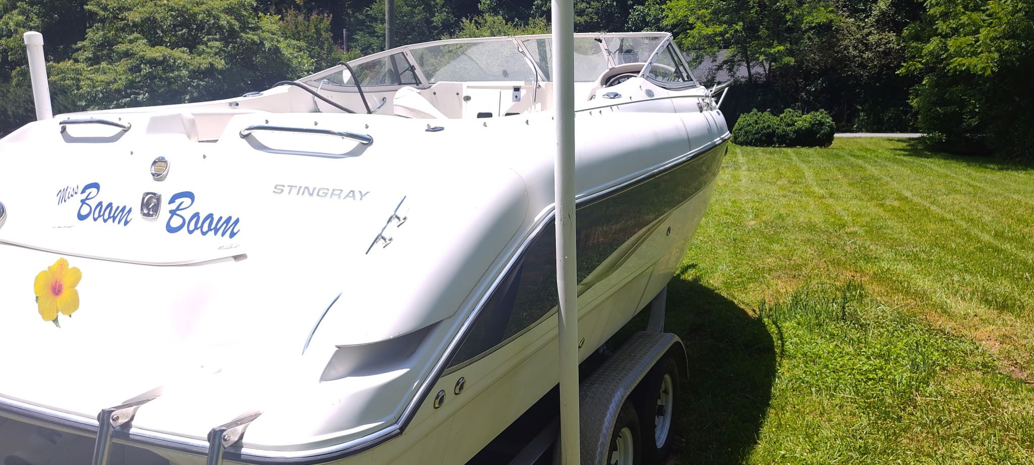 A white 2002 Stingray 240 CR boat on a trailer, set on a green lawn.