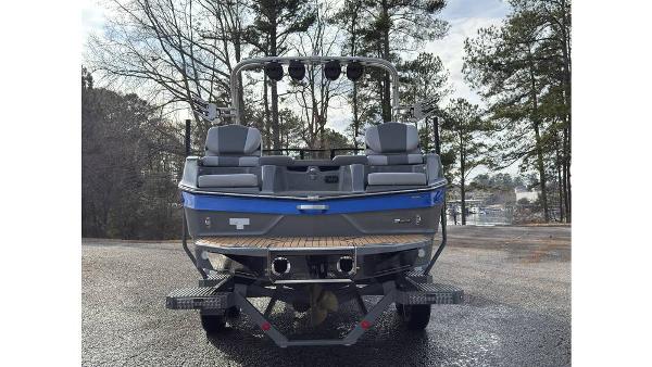 2023 MasterCraft XT22 boat, rear view, parked on a wet surface with trees in the background.
