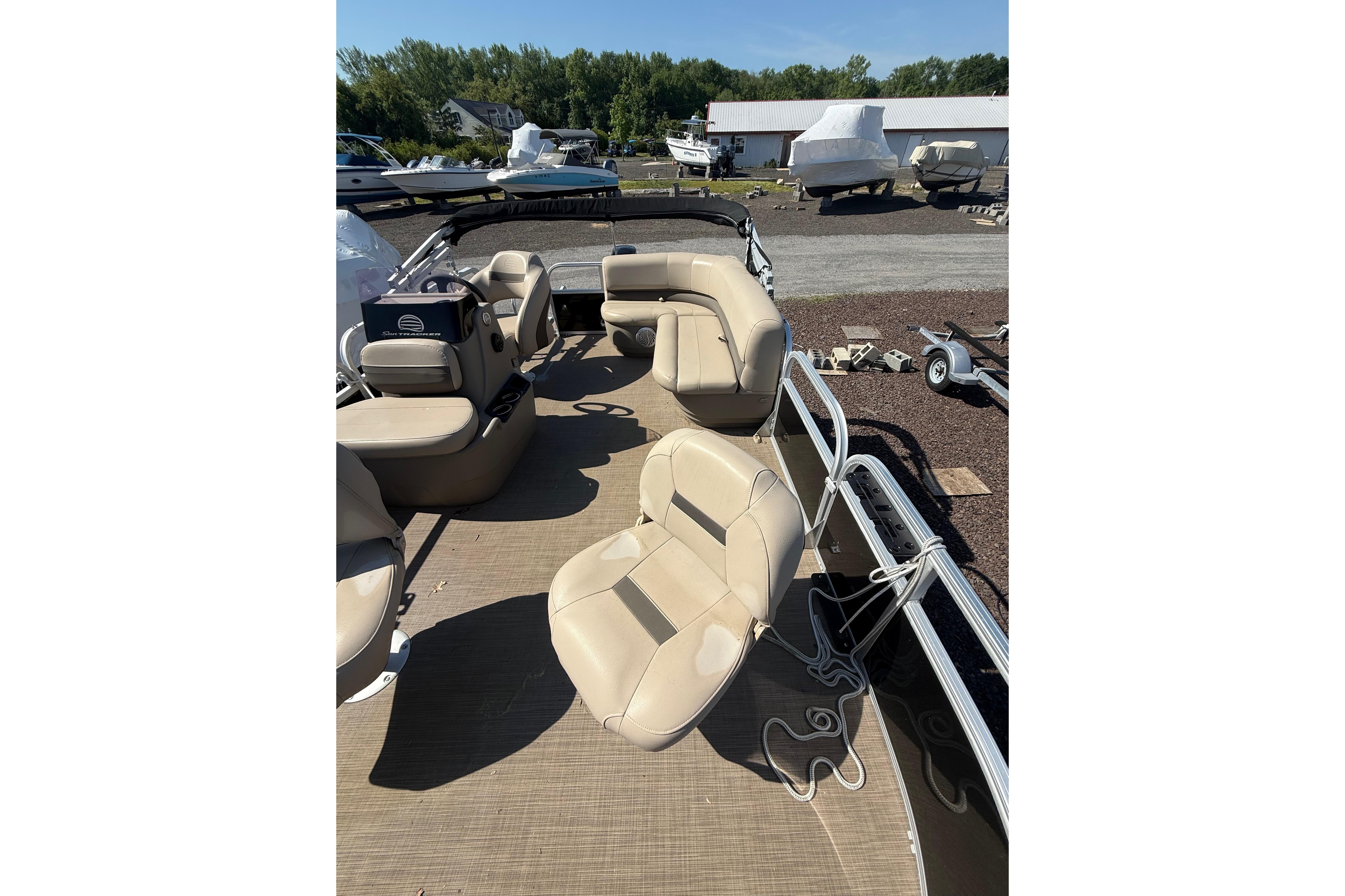 2021 Sun Tracker Bass Buggy 16 XL Select pontoon boat with beige seating, parked outdoors.