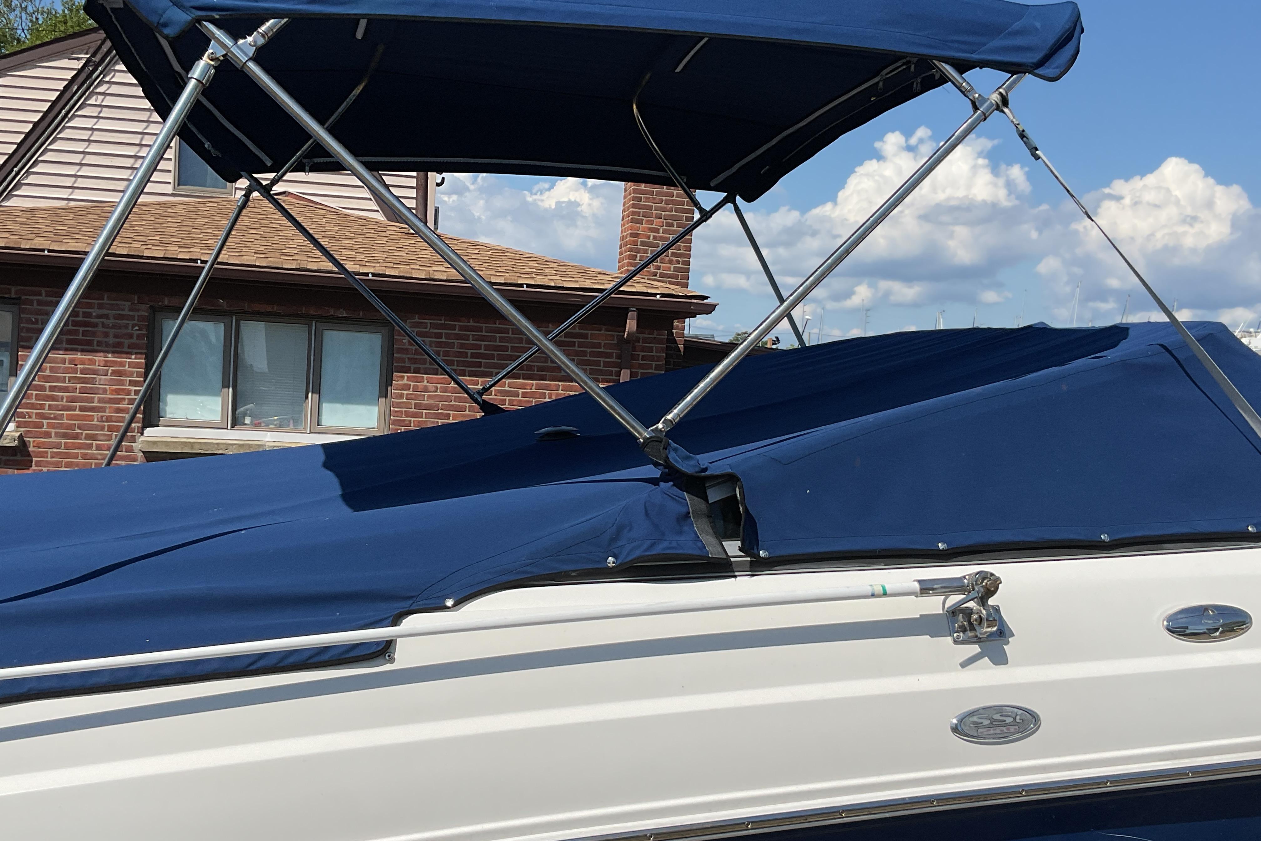 2006 Chaparral 256 SSi boat with blue canopy and cover, parked near a brick building.