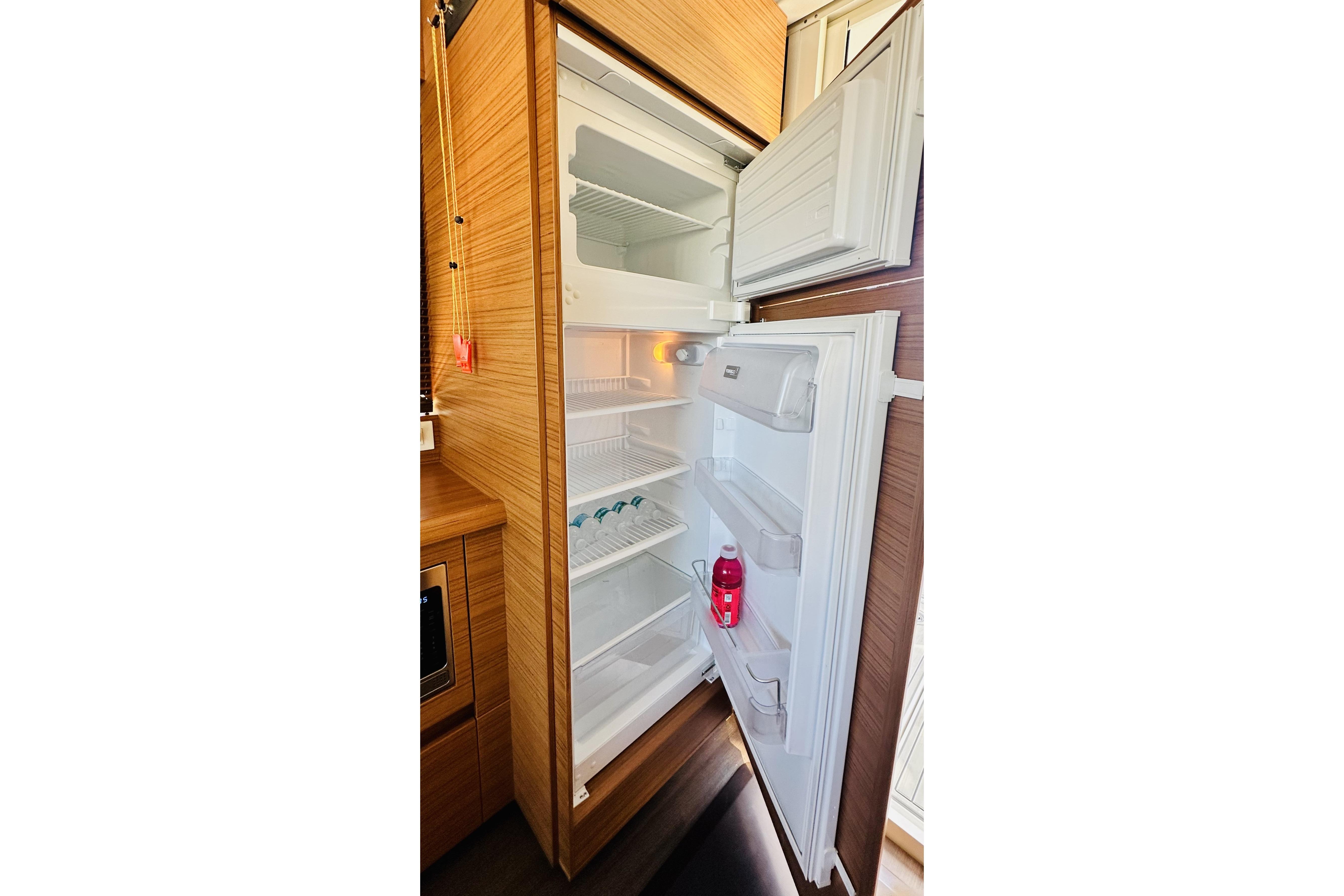 Open refrigerator inside 2021 Greenline 39 Hybrid yacht, showcasing spacious interior and wooden cabinetry.