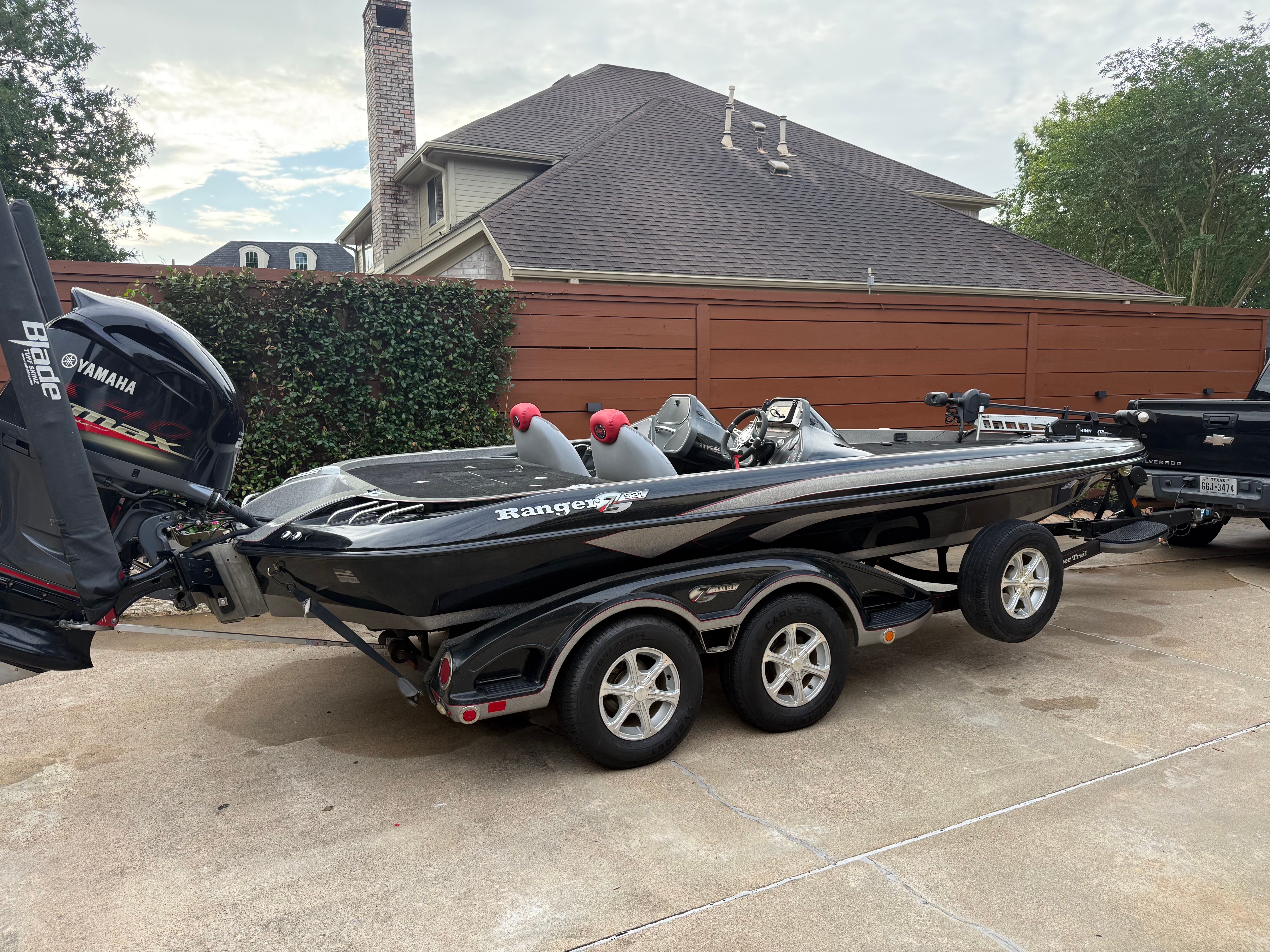 A black 2011 Ranger Z521 Comanche boat on a trailer in a driveway.