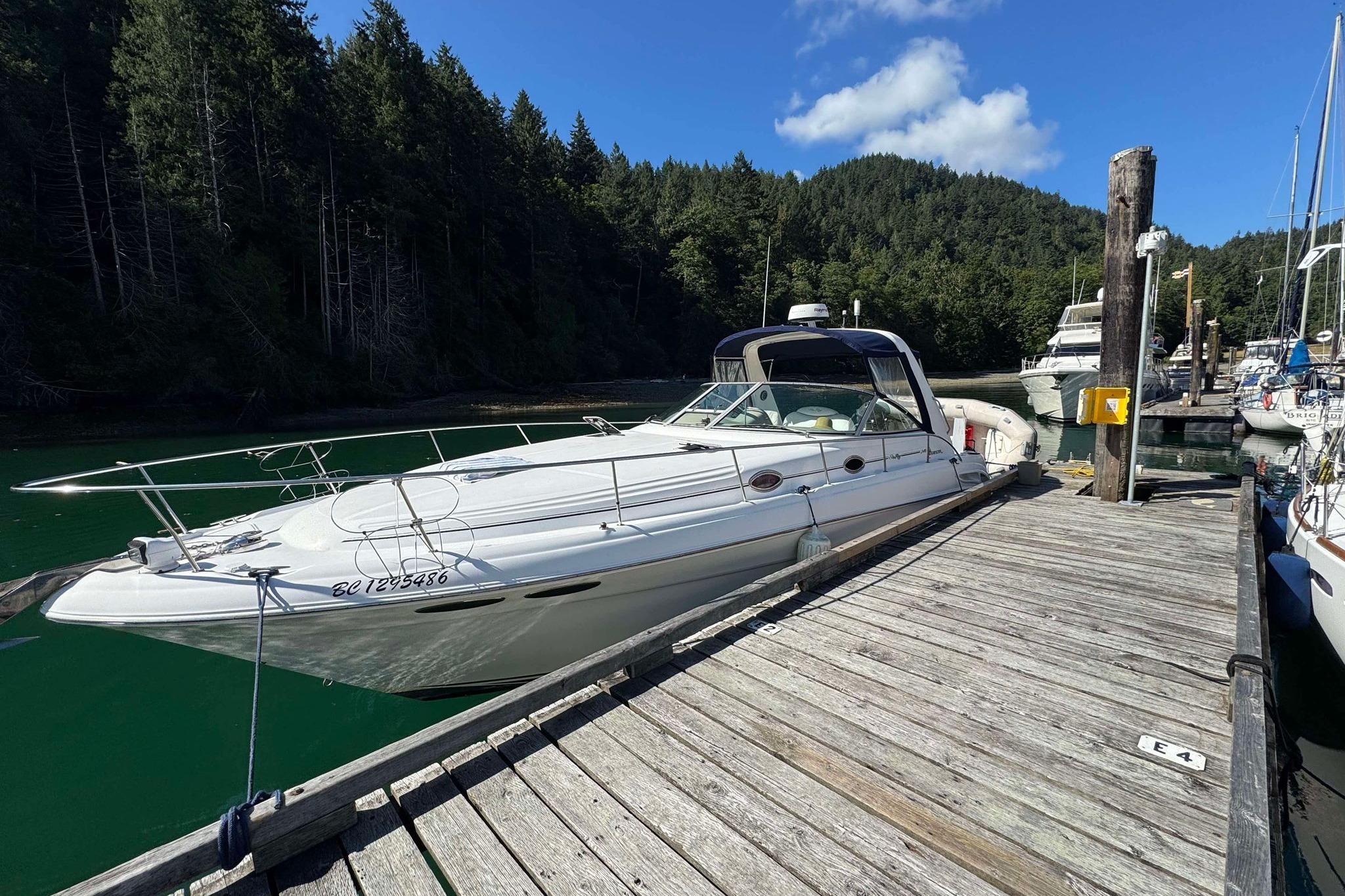 1999 Sea Ray 340 Sundancer docked in a serene marina with lush forest backdrop.