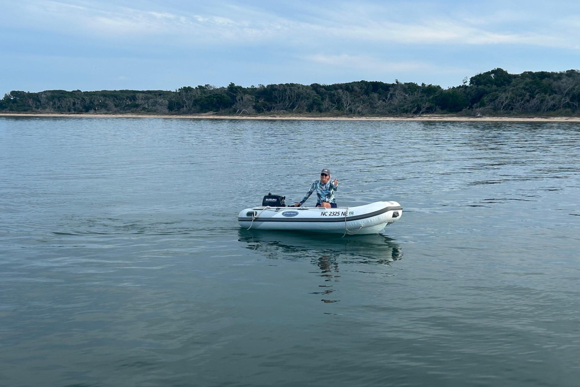 Person in a small boat on calm water near a wooded shoreline.