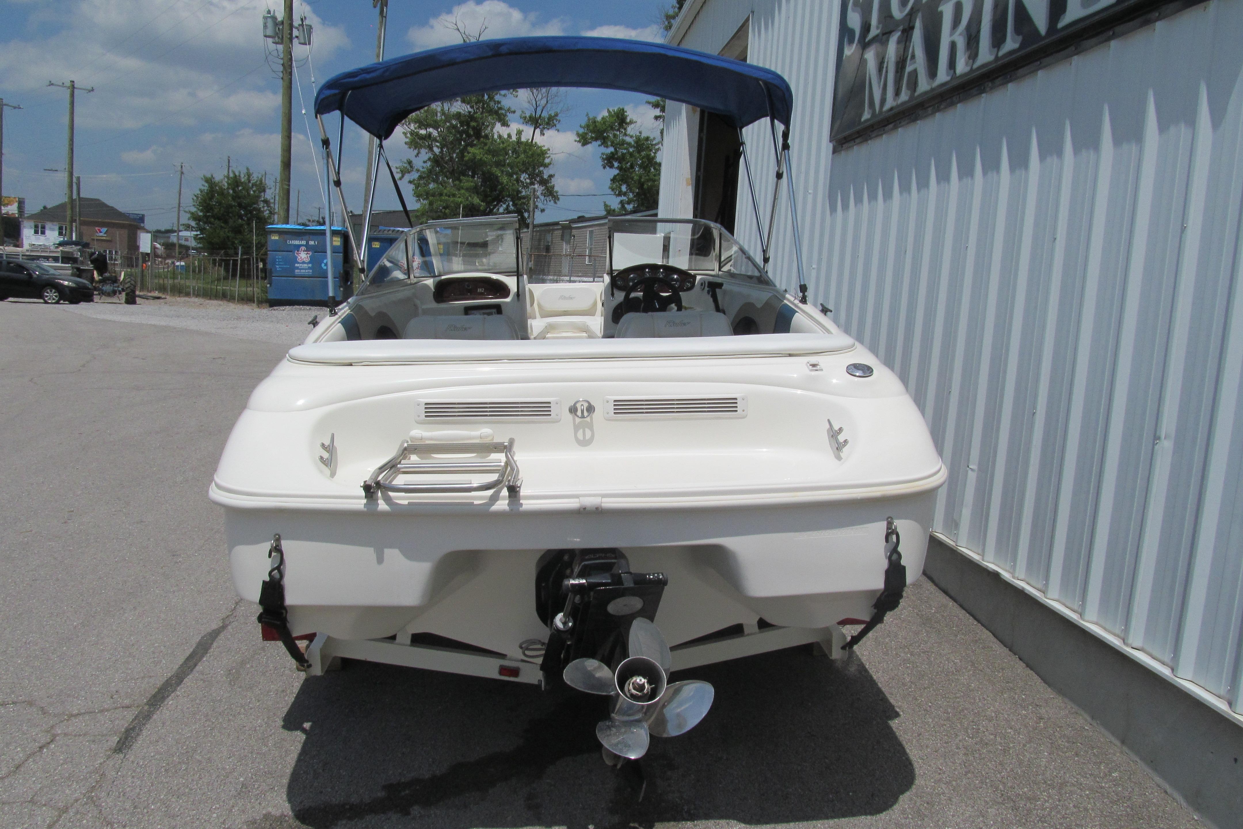 2000 Rinker boat with blue canopy, parked near a marine store.
