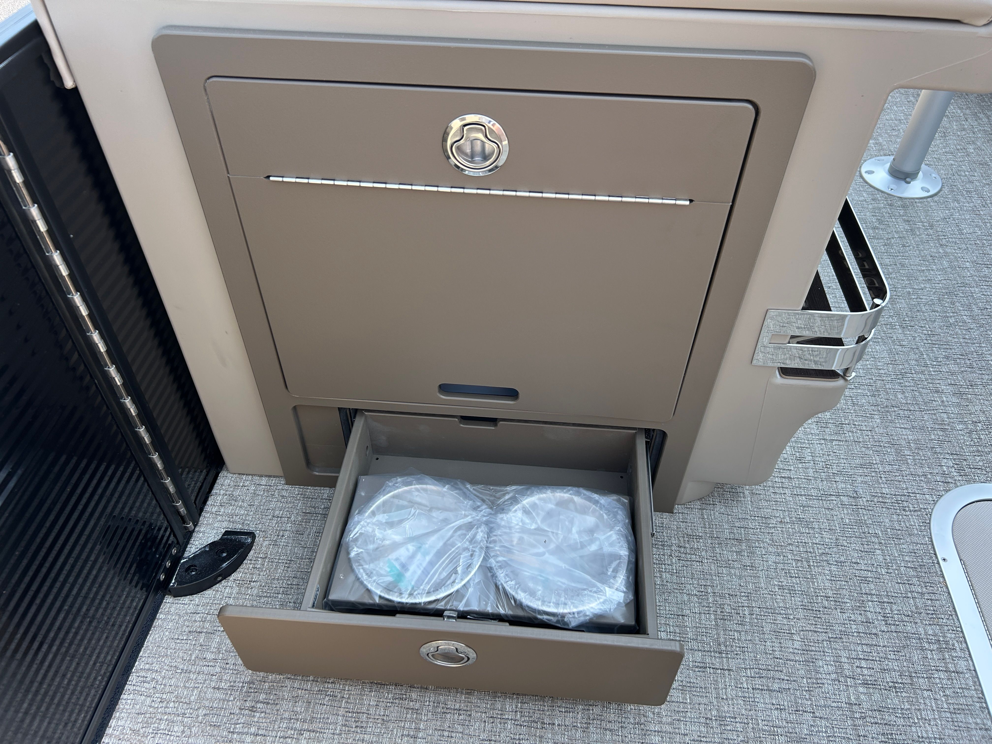 An open cabinet on a boat with two round items in a drawer.