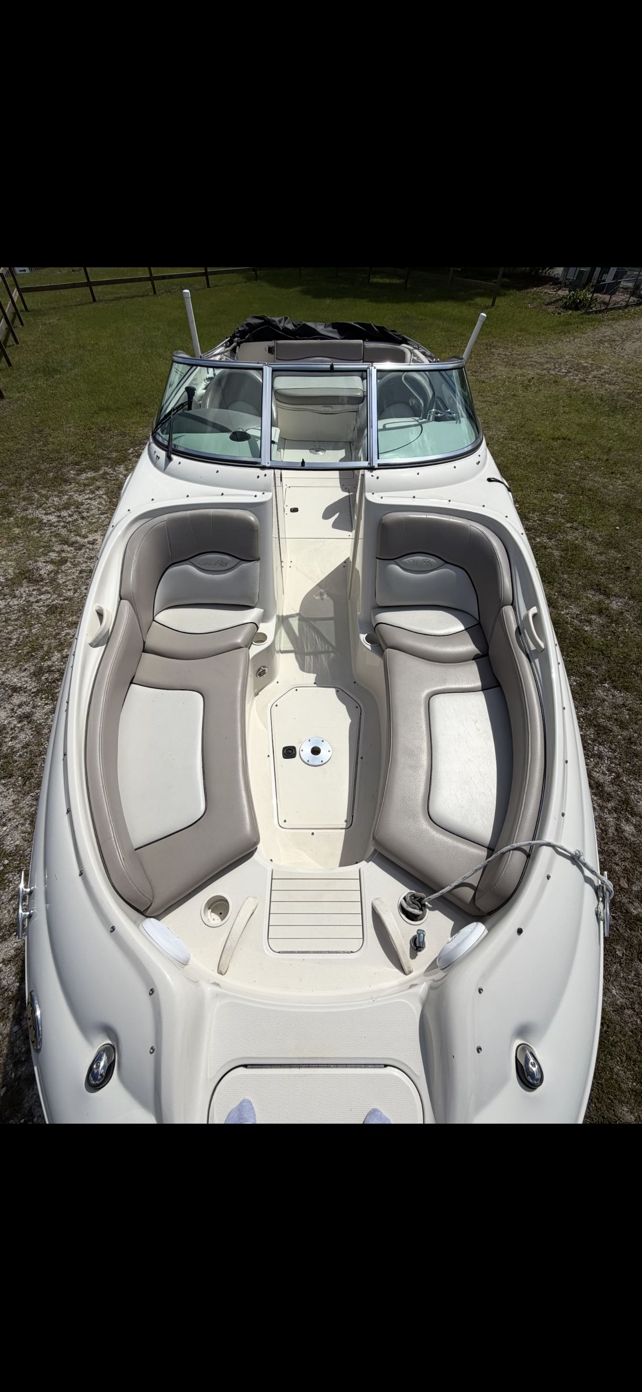 A white boat with beige seating is on dry grass.