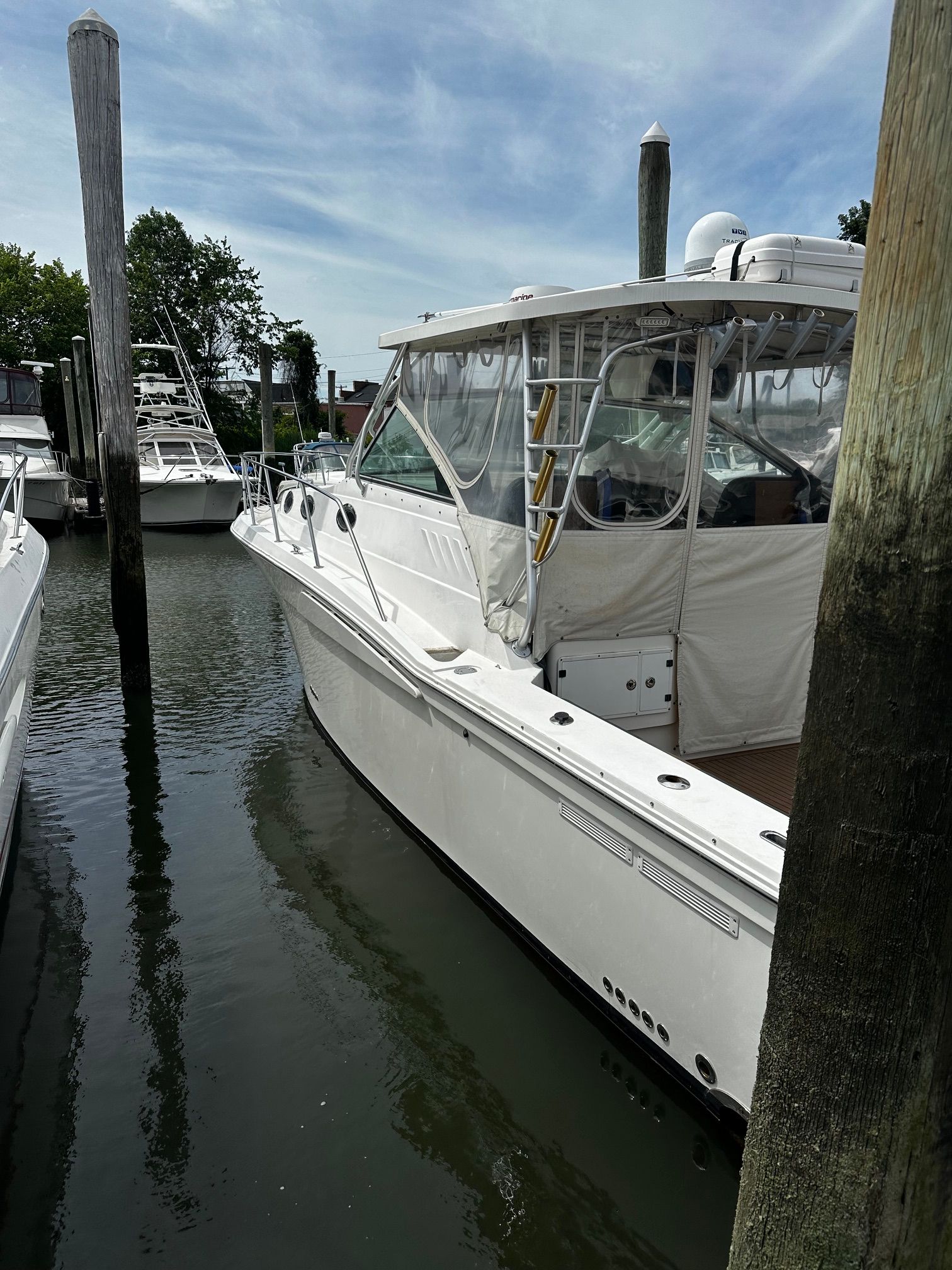 A white boat is docked in a calm harbor, surrounded by wooden posts.