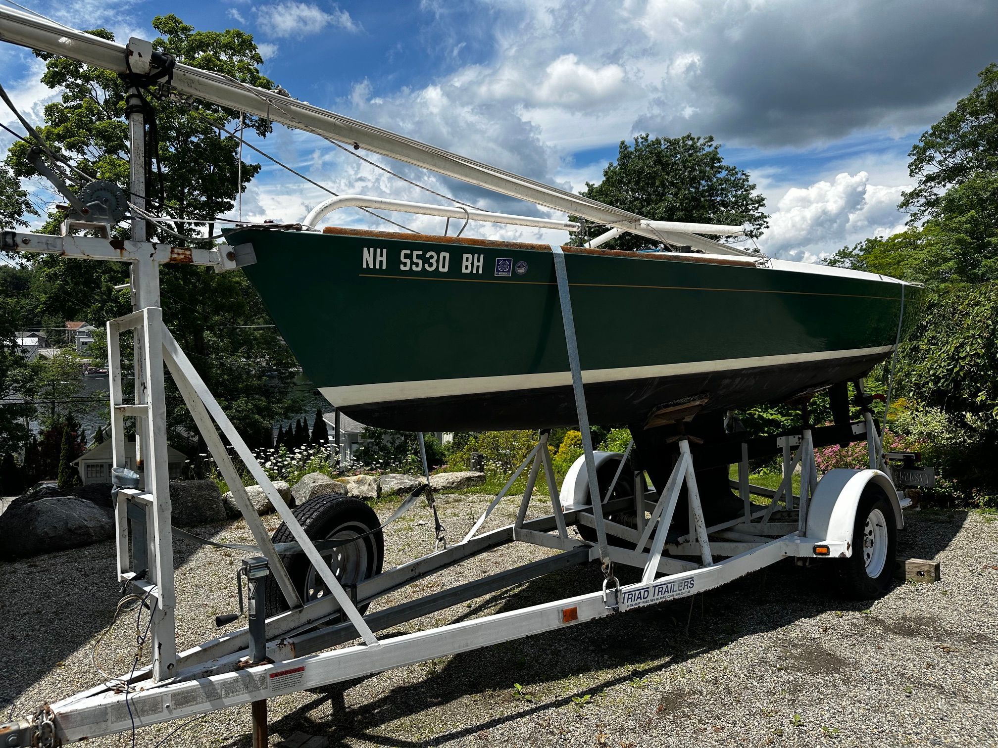 Alerion Express 20 sailboat on a trailer, surrounded by trees and a cloudy sky.