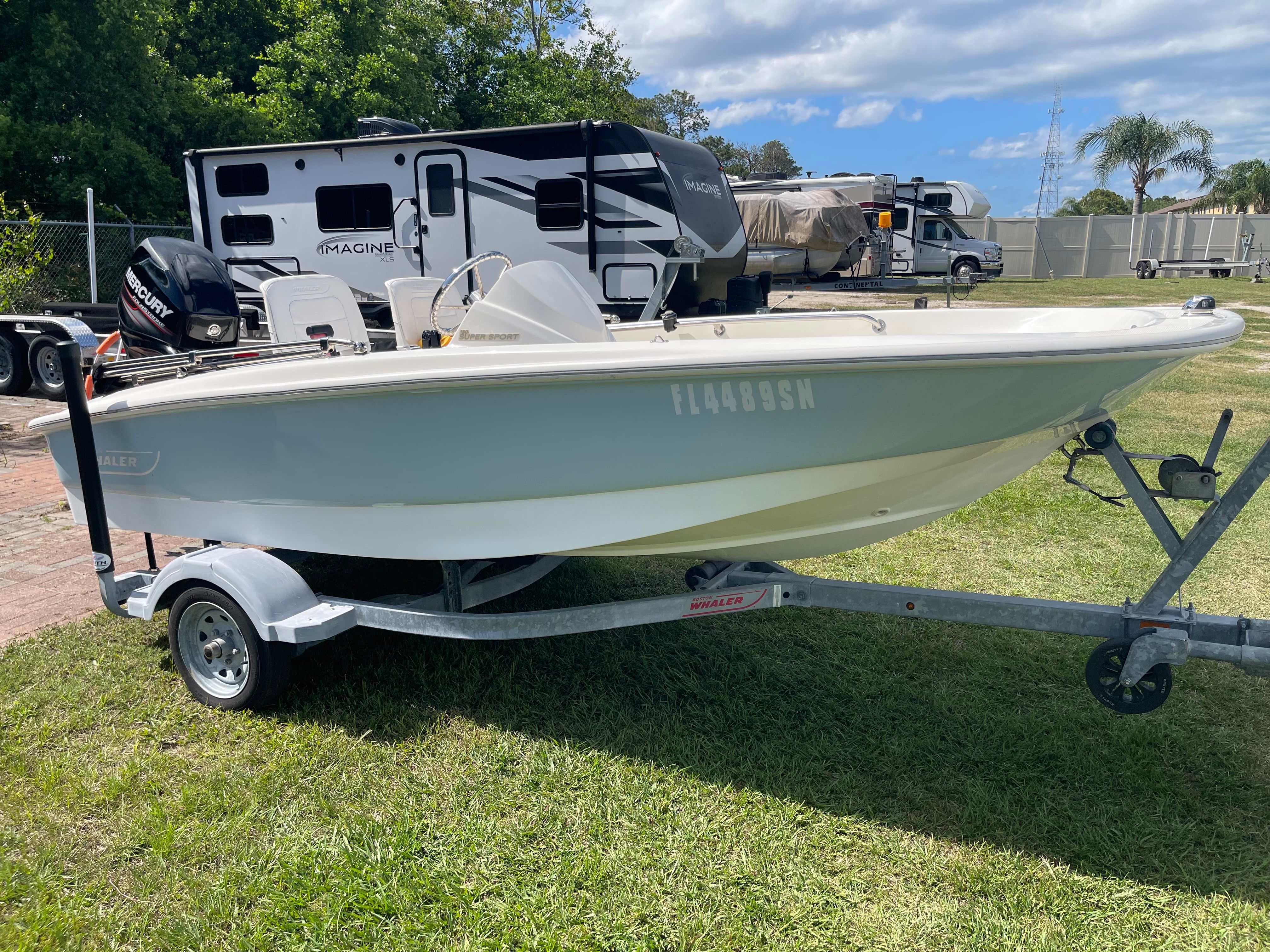 A 2017 Boston Whaler 130 Super Sport on a trailer, parked on grass.