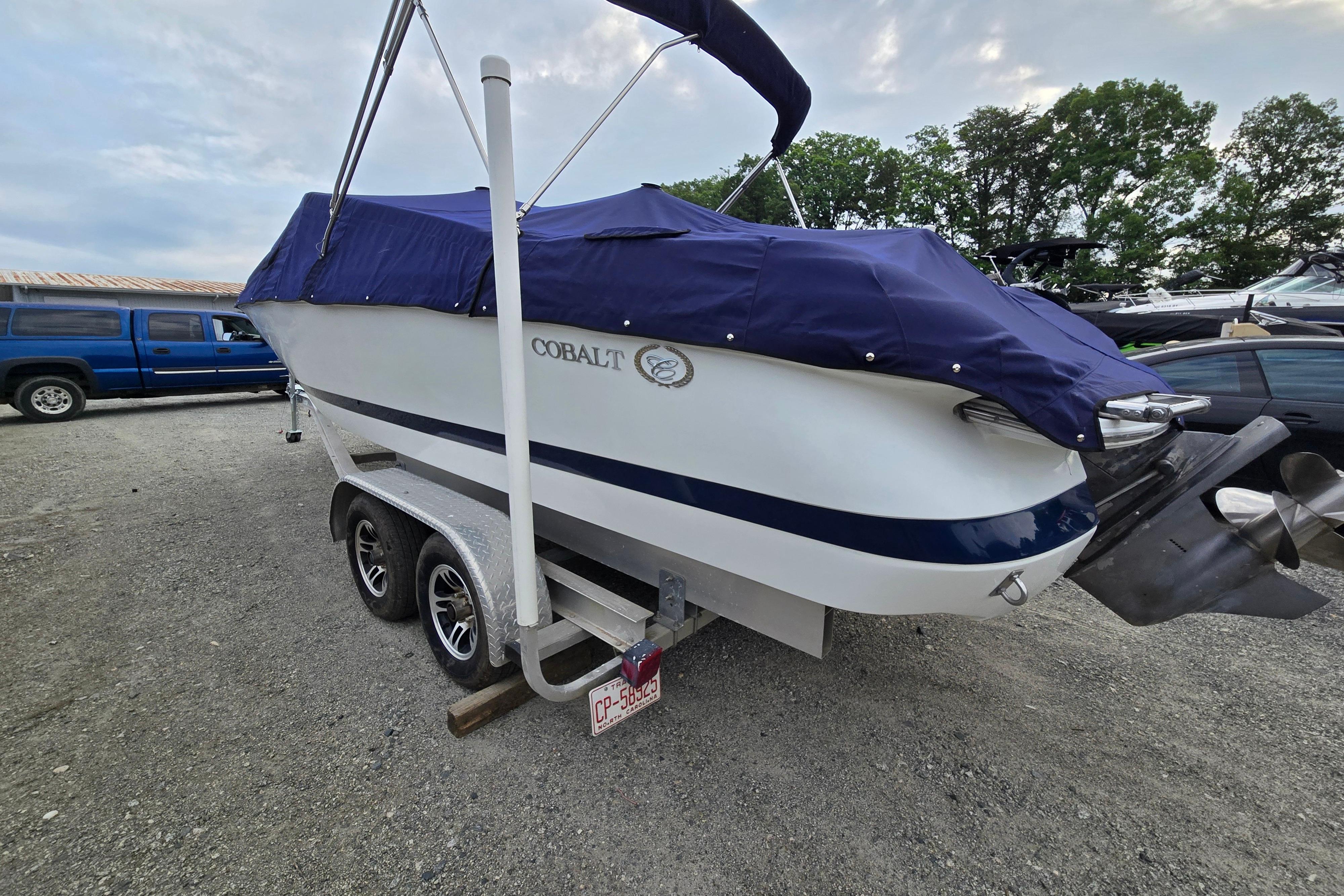 Covered 2000 Cobalt 246 boat on trailer, parked outdoors with trees in background.