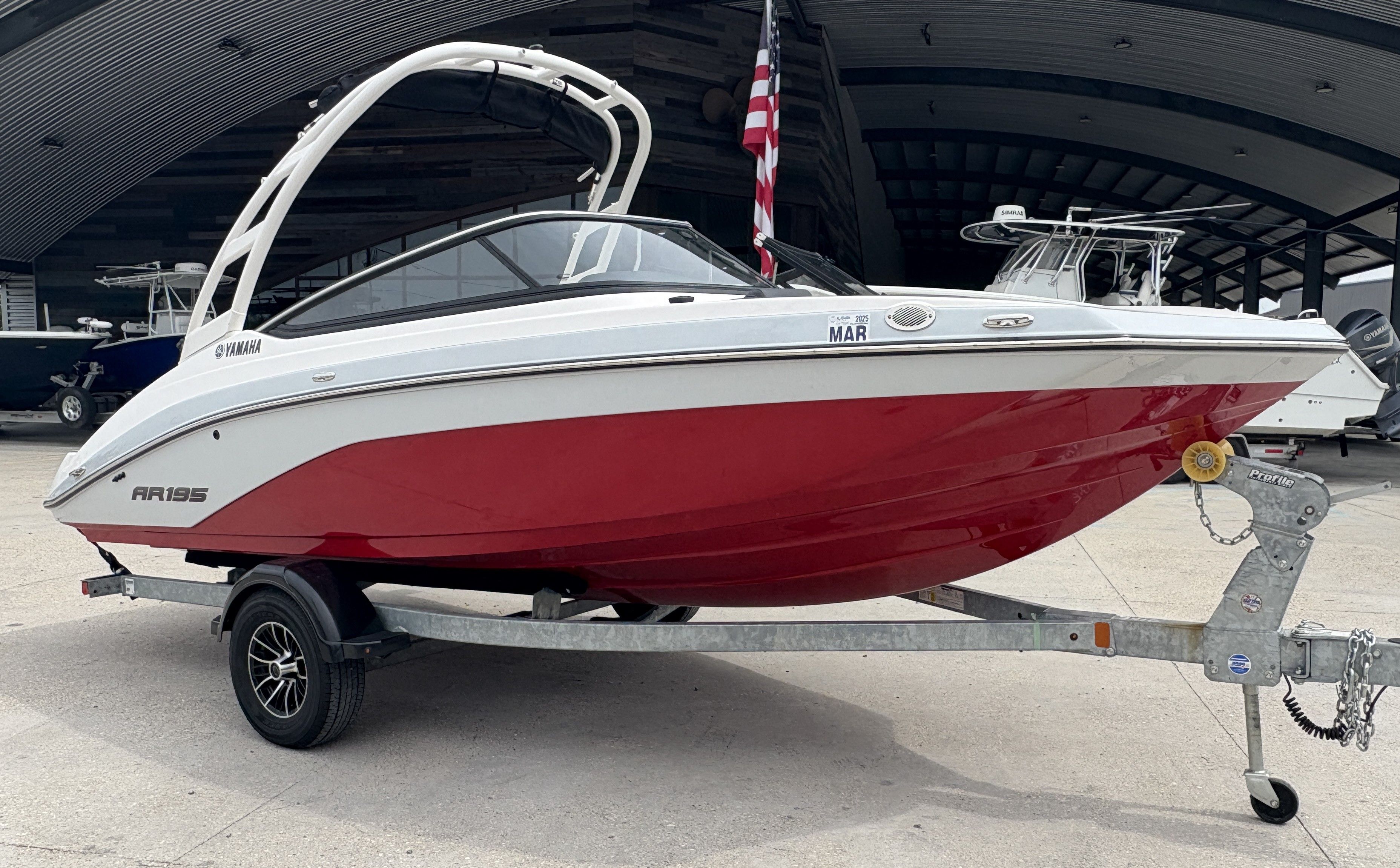 2024 Yamaha AR 195 boat with red hull on a trailer, parked outdoors.