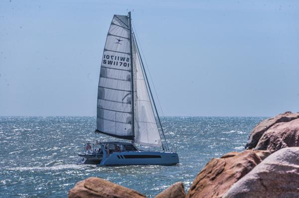 2025 Seawind 1170 sailing near rocky coastline on a sunny day.