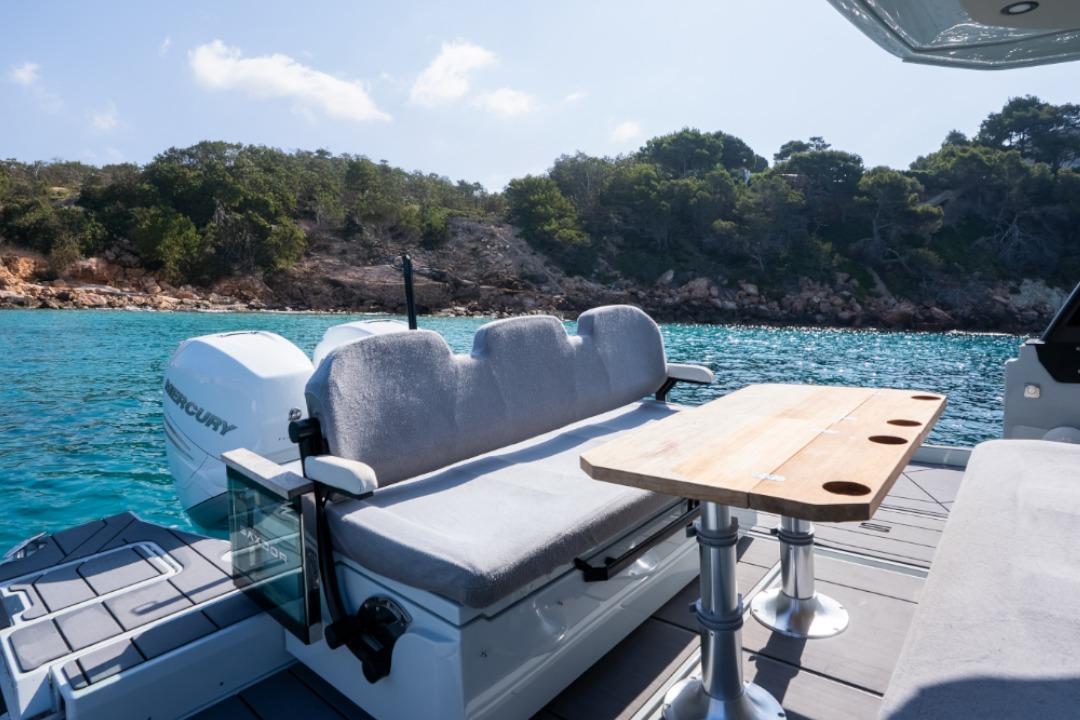 2023 Saxdor 320 GTO boat with seating and table, anchored near a scenic coastline.