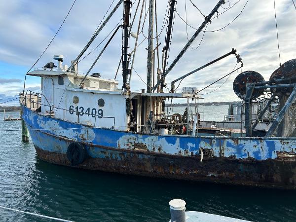 Old 1979 custom steel trawler dragger docked, showing weathered blue and white paint.