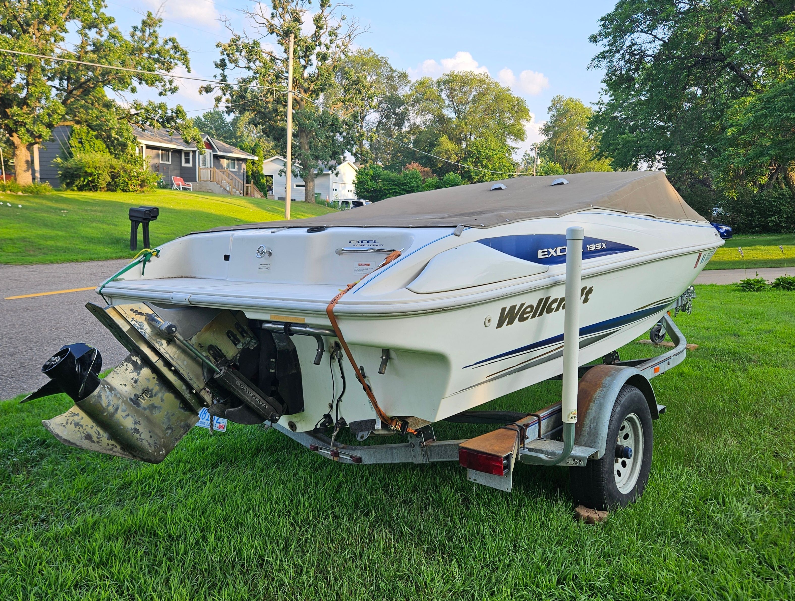A 1996 Wellcraft Excel boat on a trailer, parked on a grassy lawn.