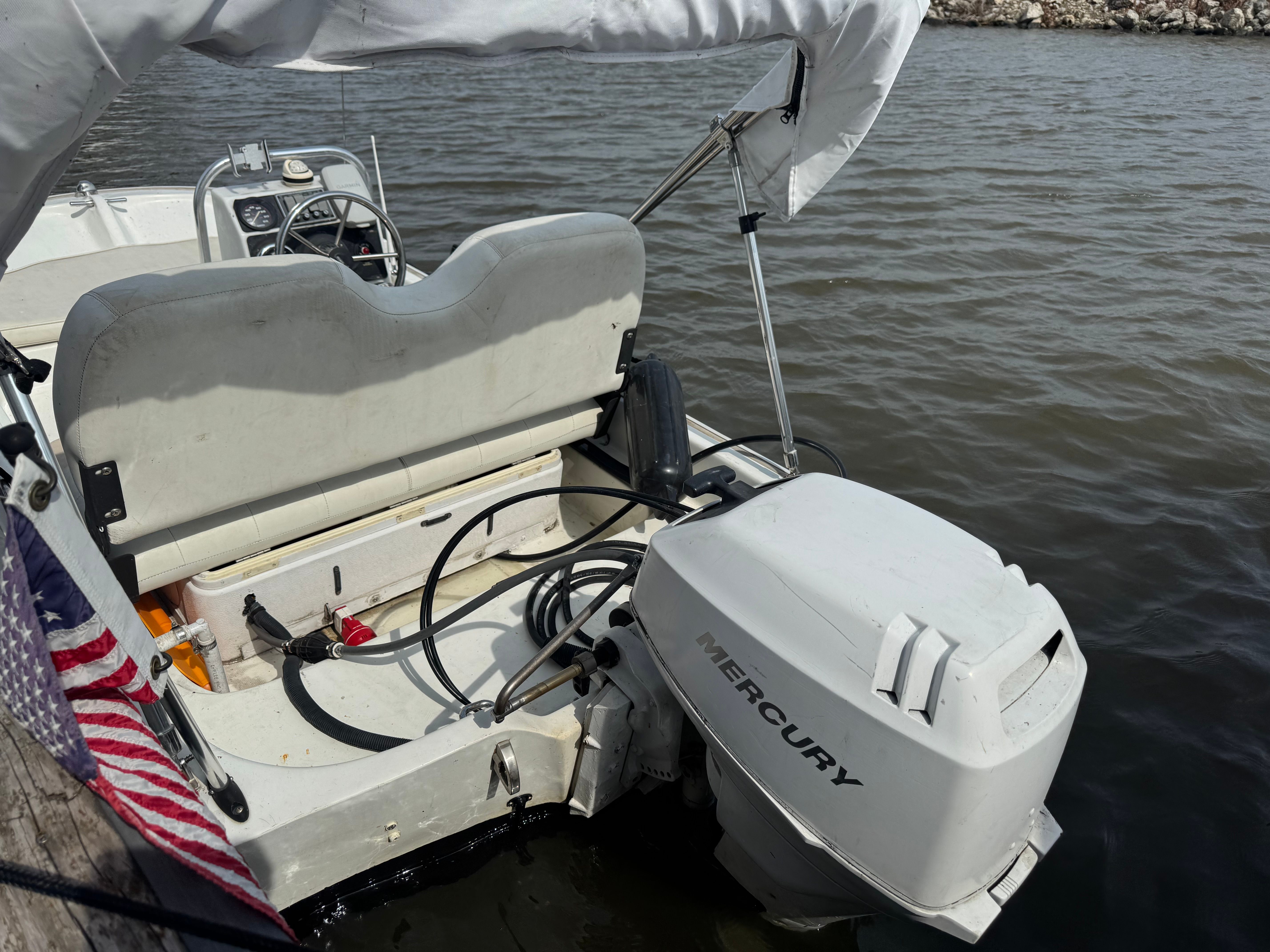 A boat with a Mercury outboard motor is docked on the water. It features a white bench seat.
