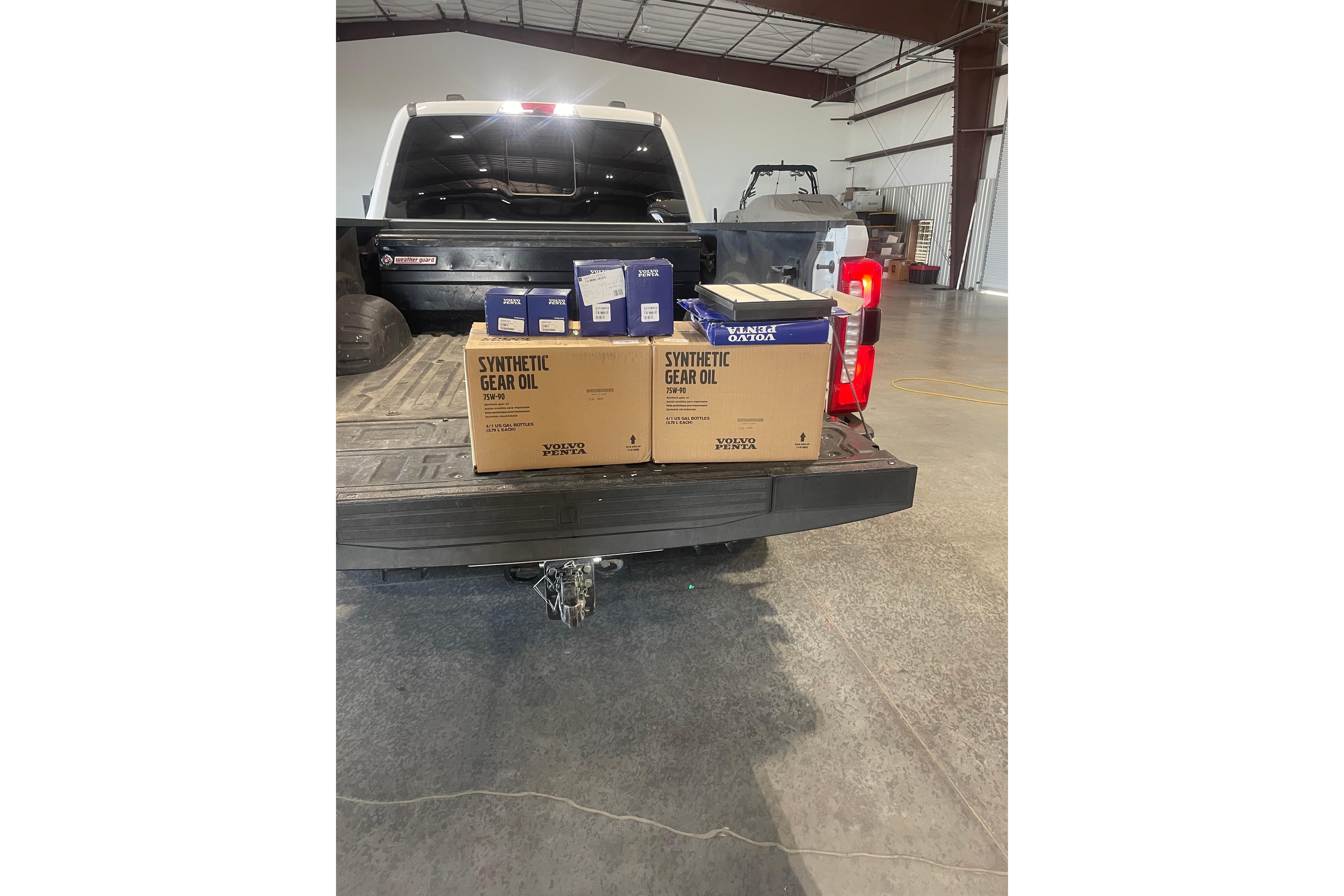 Pickup truck bed with synthetic gear oil boxes, Volvo Penta brand, in a warehouse setting.