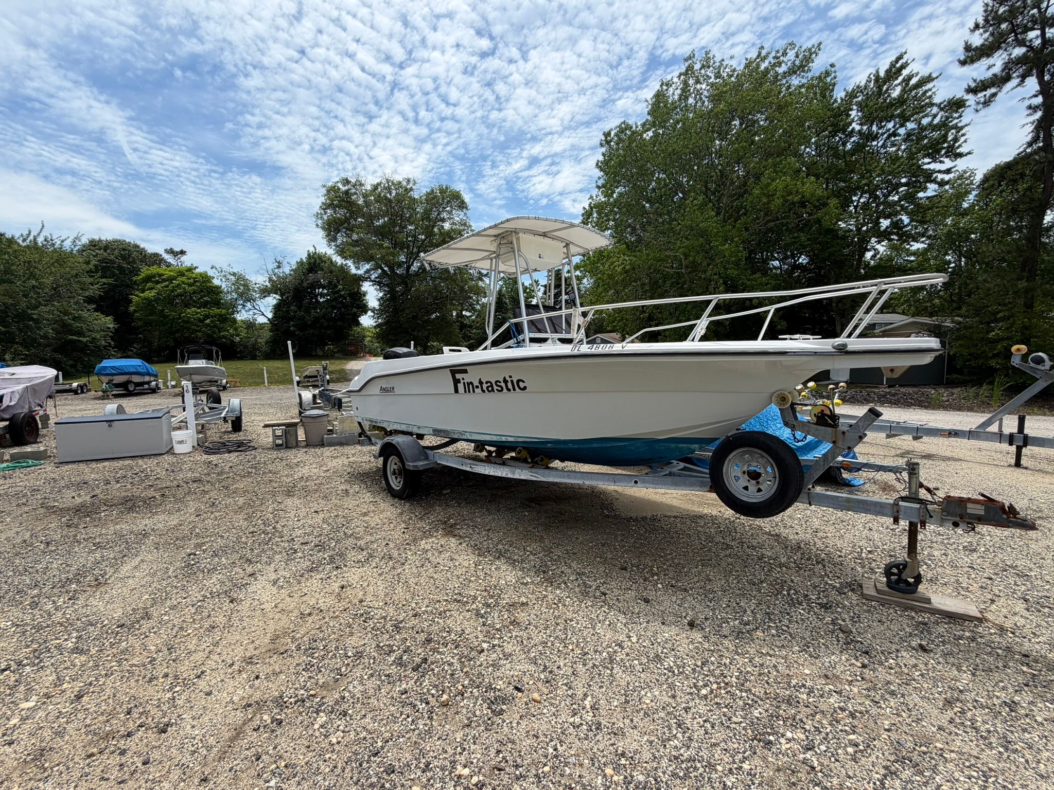 An Angler boat on a trailer, surrounded by trees and gravel ground.
