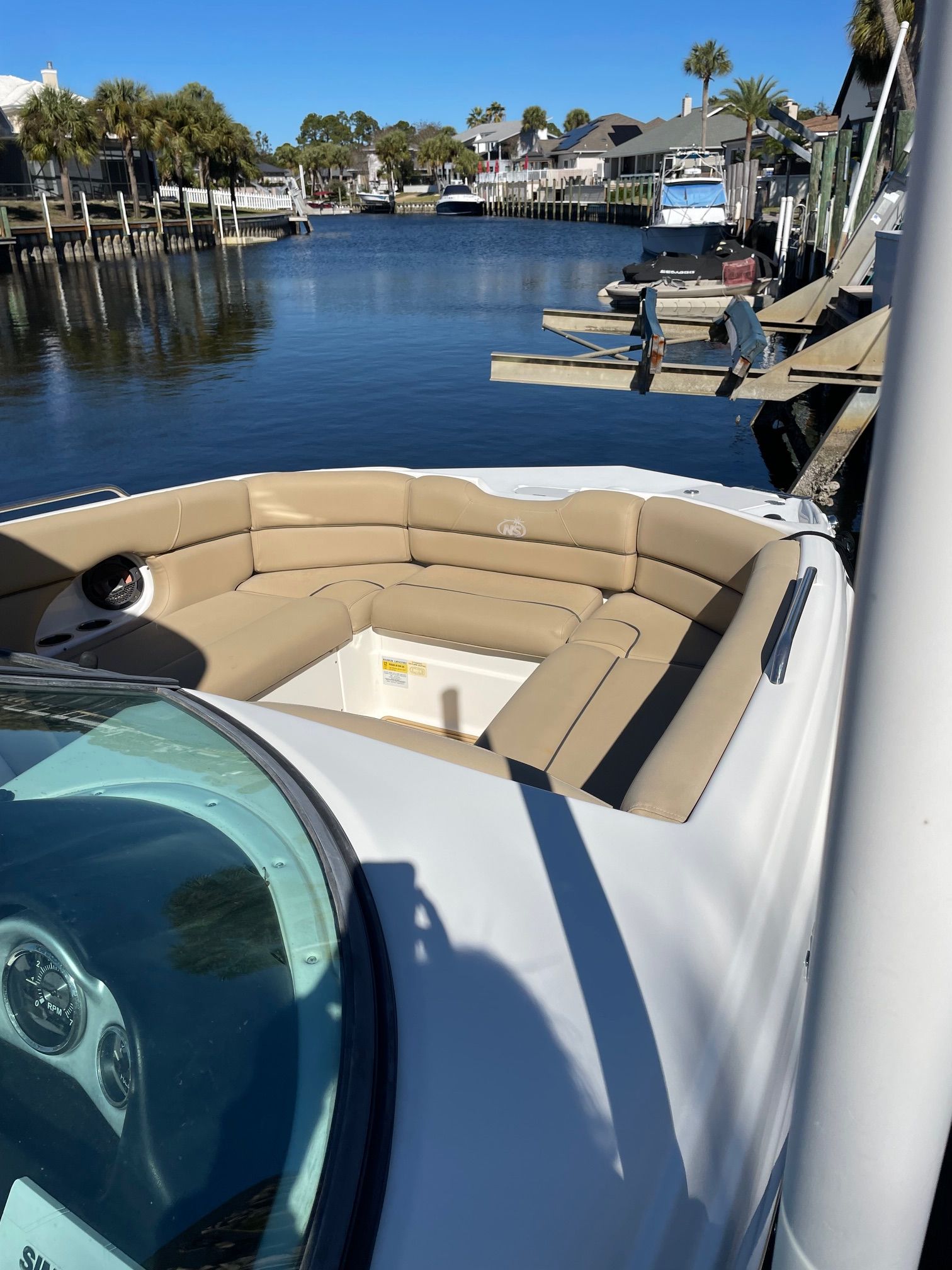 2019 NauticStar 243DC Sport Deck in a calm harbor with palm trees in the background.