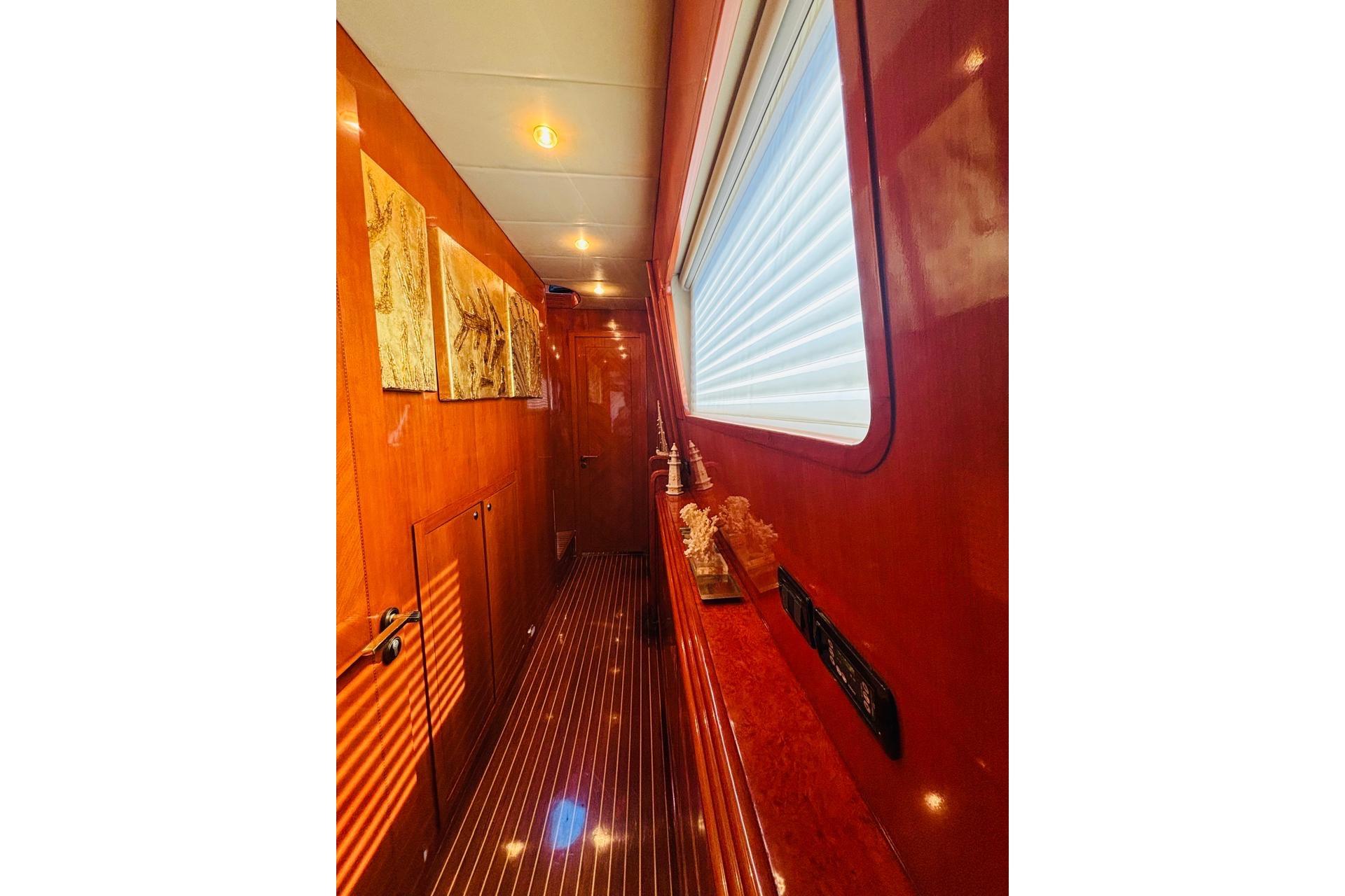Luxurious wooden interior hallway of 2000 Falcon 100 yacht with artwork and window blinds.