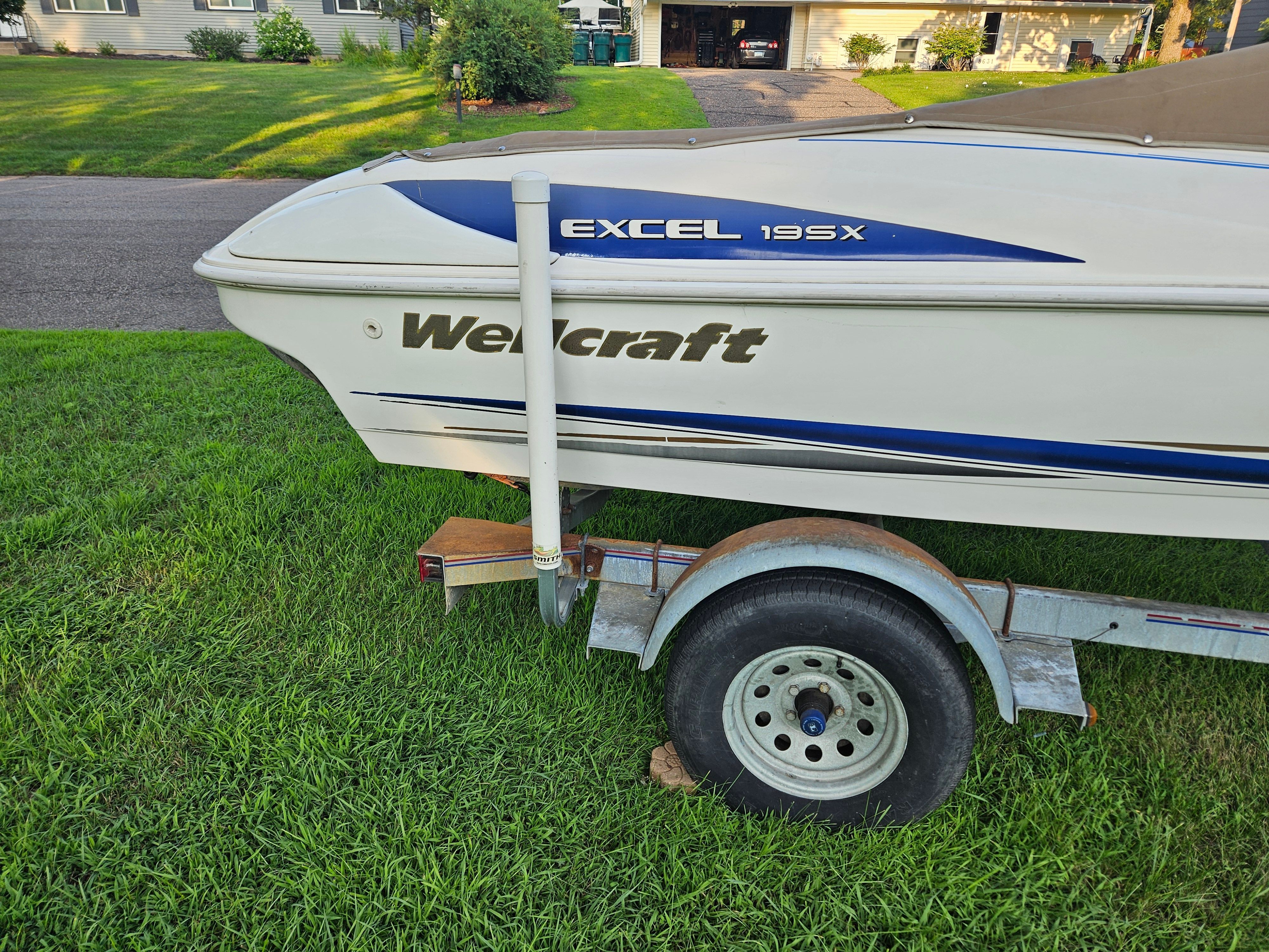 A 1996 Wellcraft Excel 195X boat on a trailer, parked on a grassy area.