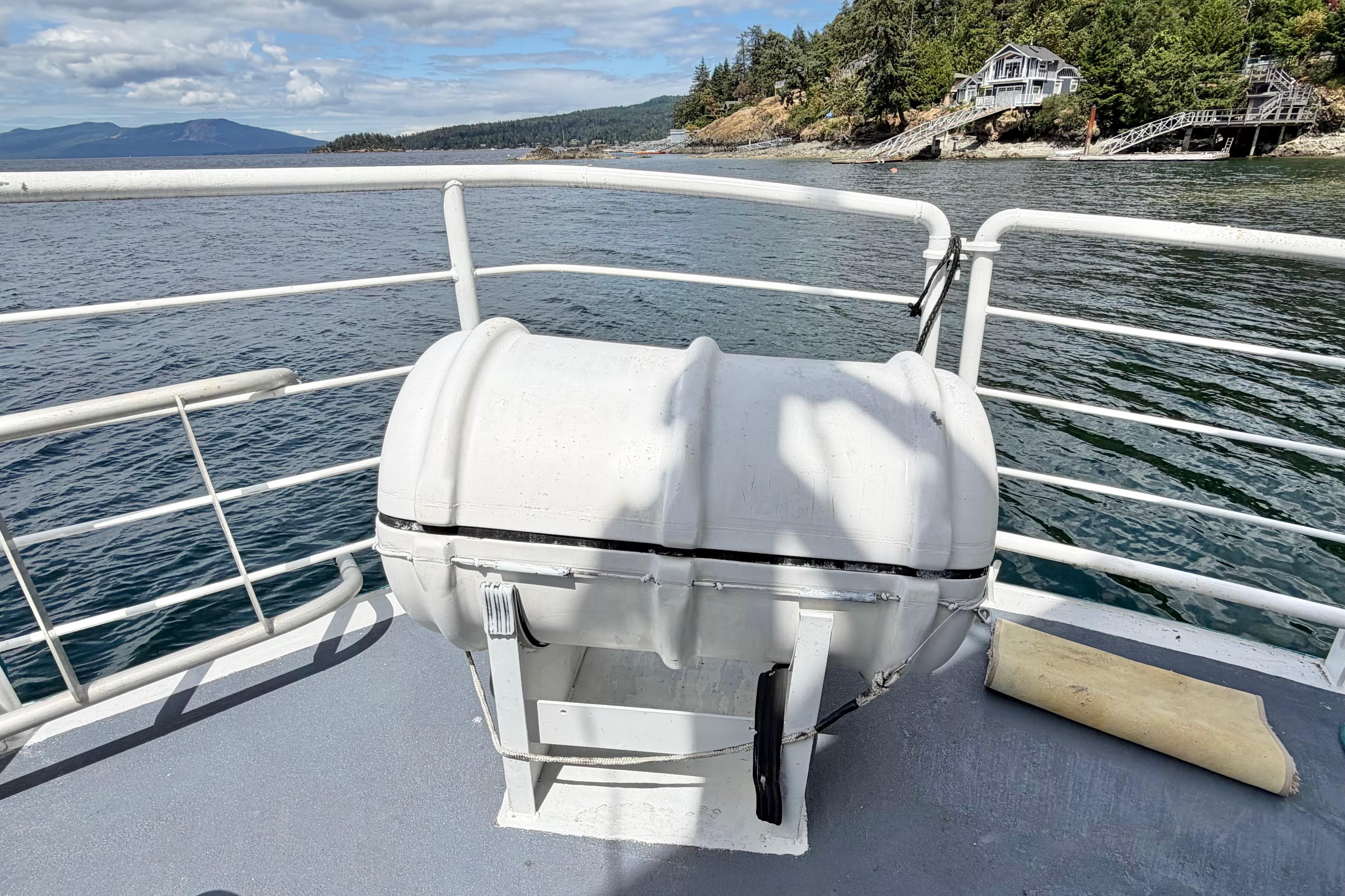 Houseboat deck with life raft, ocean view, and coastal landscape in the background.