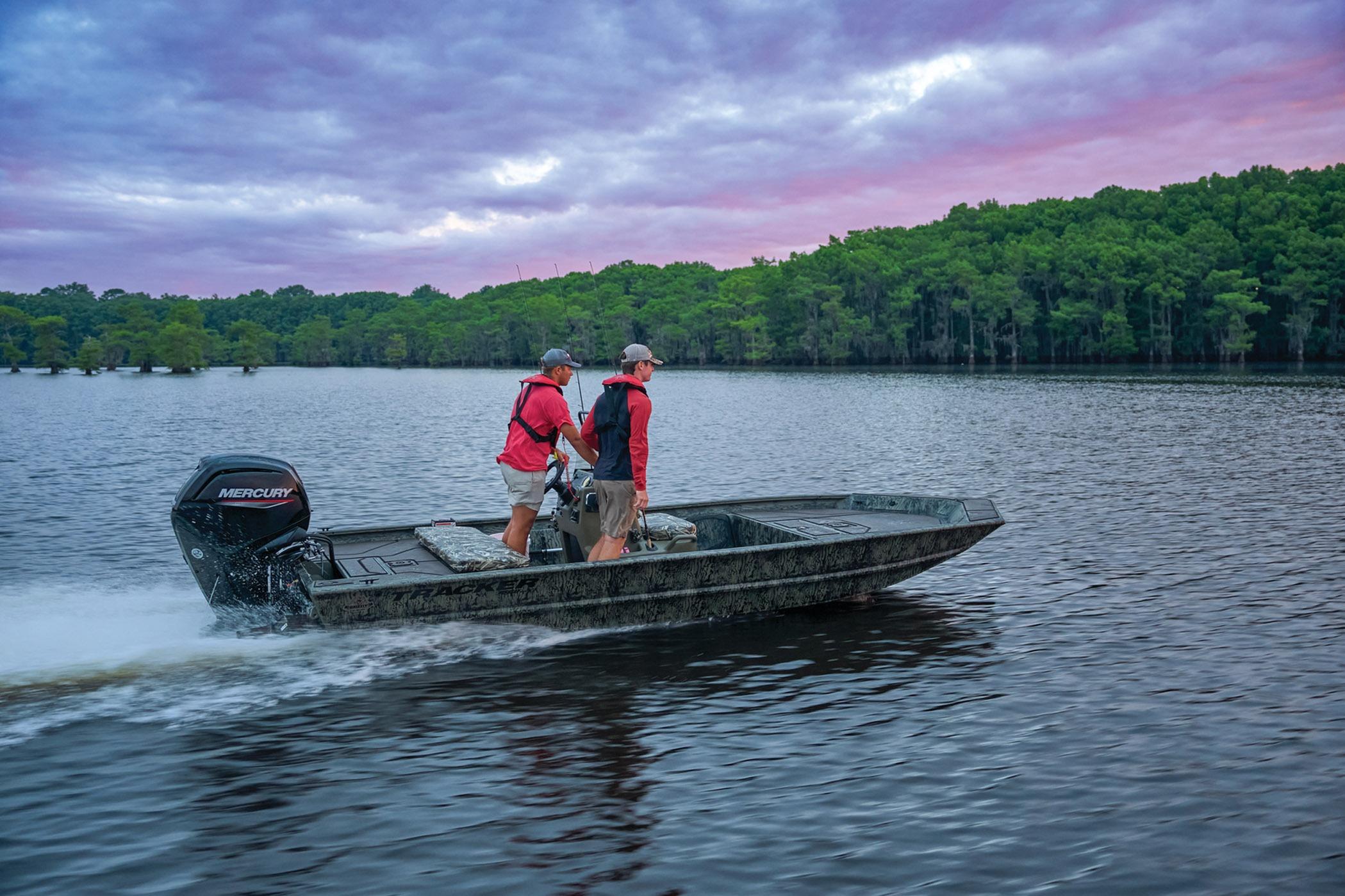 2026 Tracker Grizzly 1860 CC boat cruising on a scenic lake at sunset.