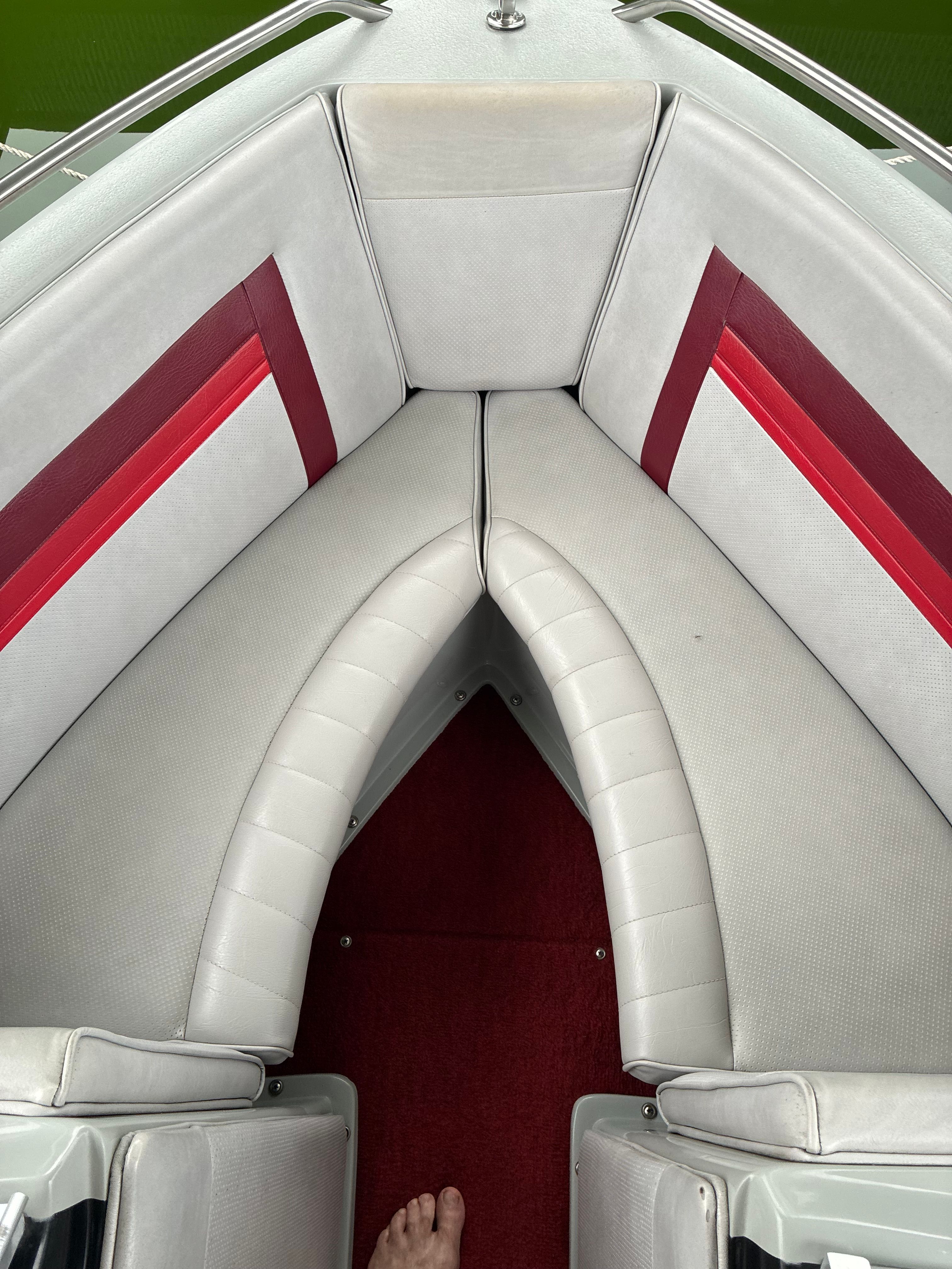 Interior view of a boat with gray and red upholstery in the bow area.