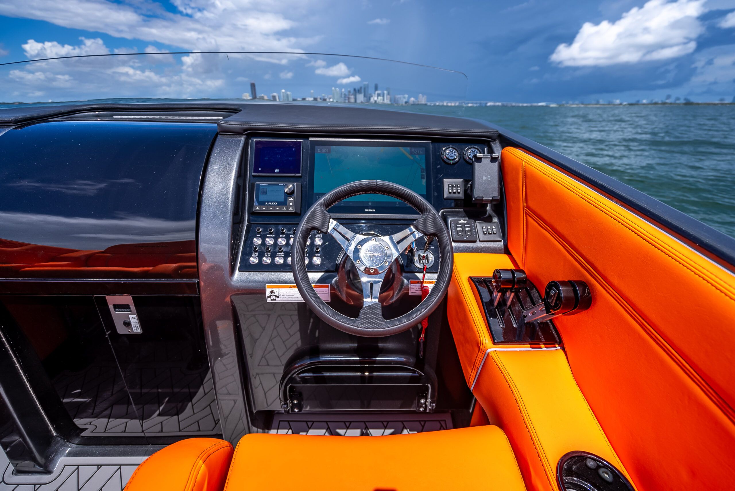 The cockpit of a modern sport boat with orange seats and a sleek helm.